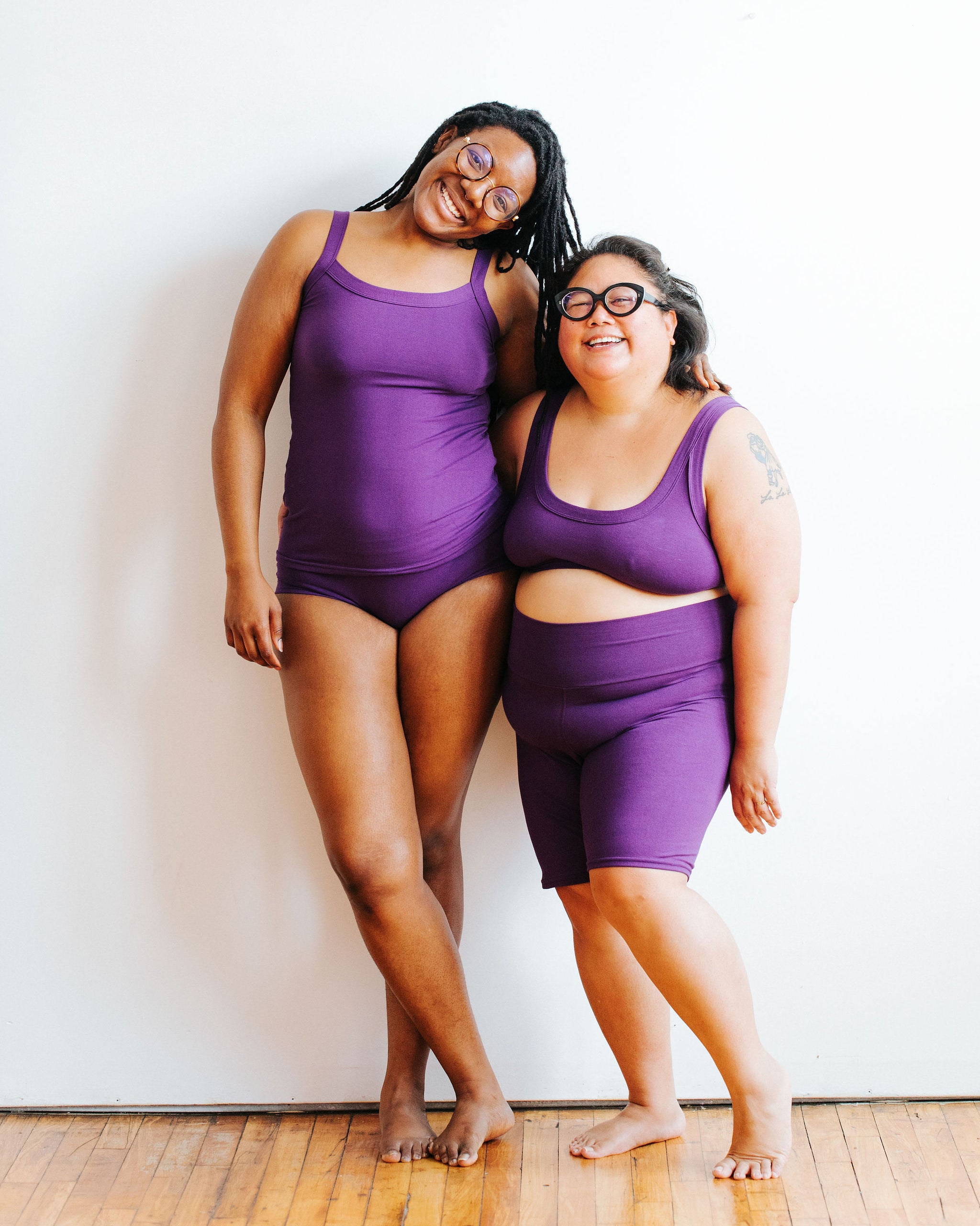 Two models smiling together wearing a variety of items in our Deep Amethyst solid color.