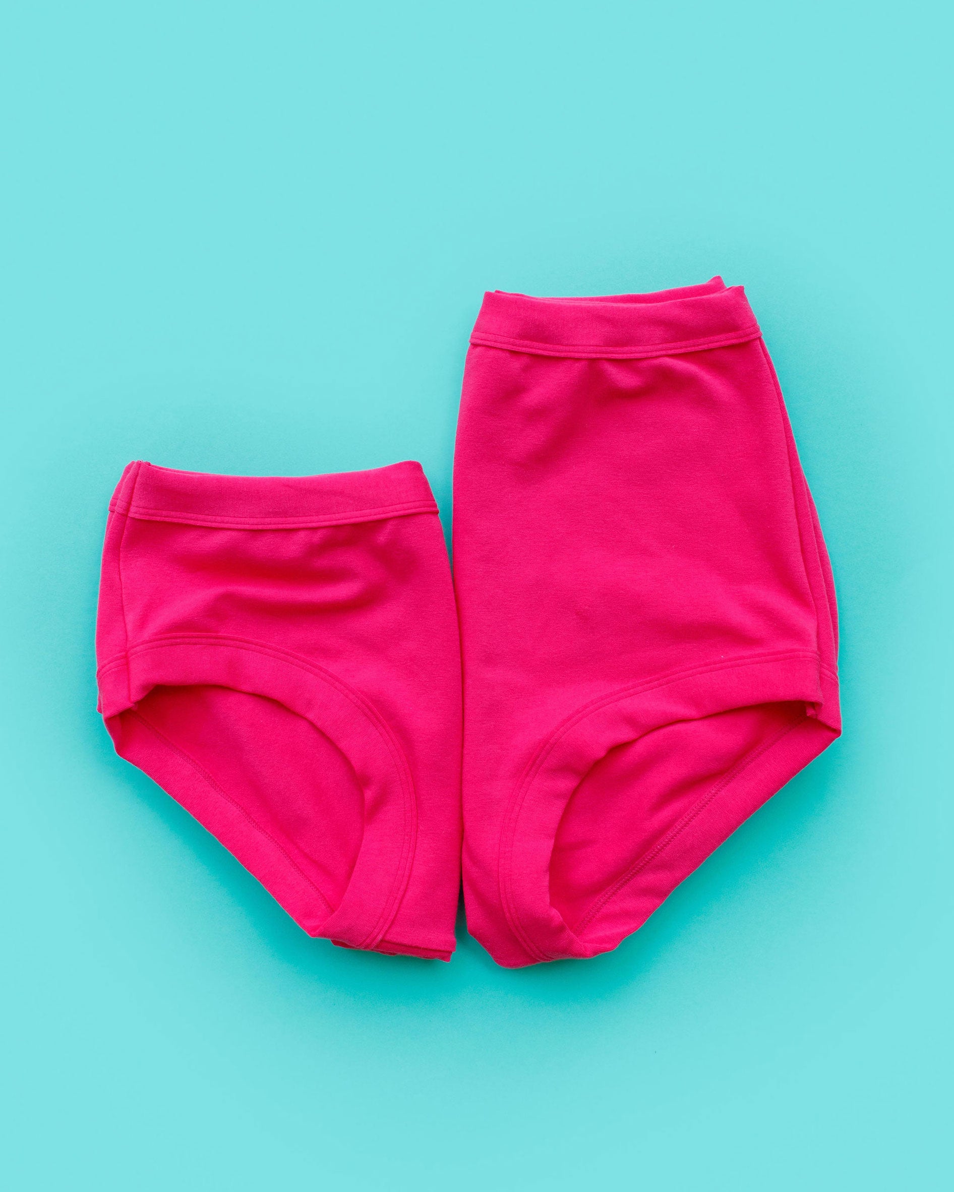 Flat lay of two folded Thunderpants Hipster style and Sky Rise style underwear in a hot pink color.