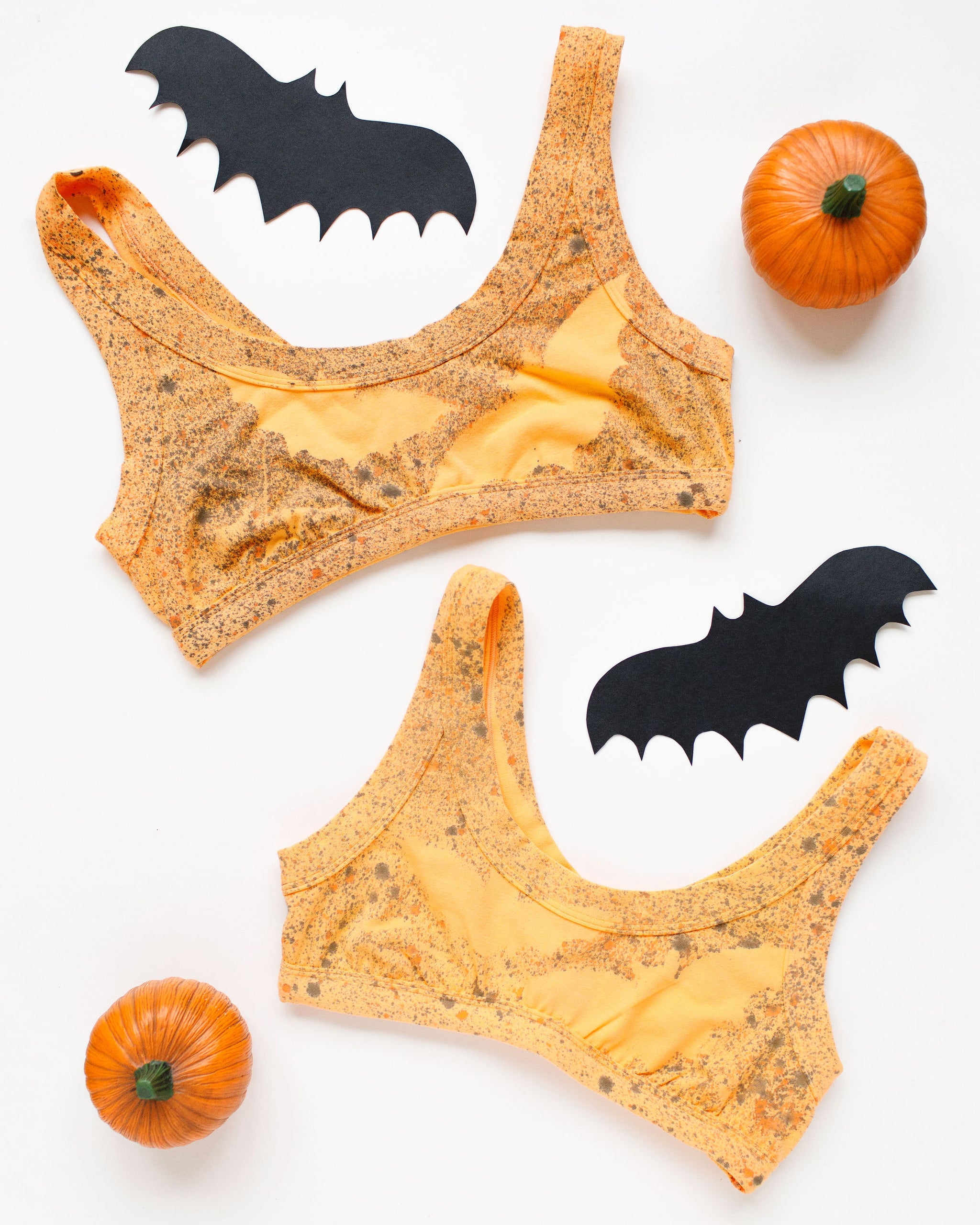 Flat lay of two Thunderpants Bralettes in Orange Sherbet with bats hand painted.