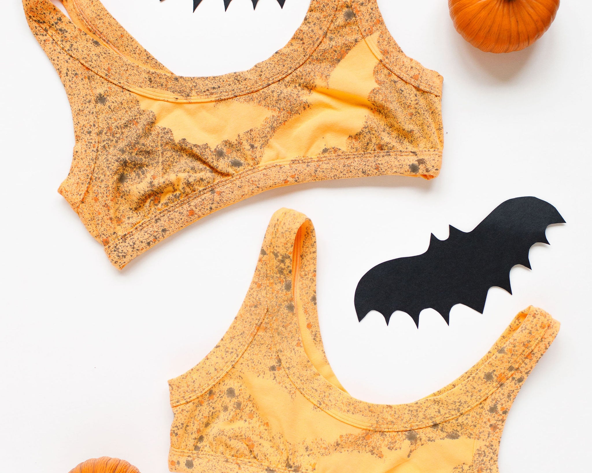 Flat lay of two Thunderpants Bralettes in Orange Sherbet with bats hand painted.