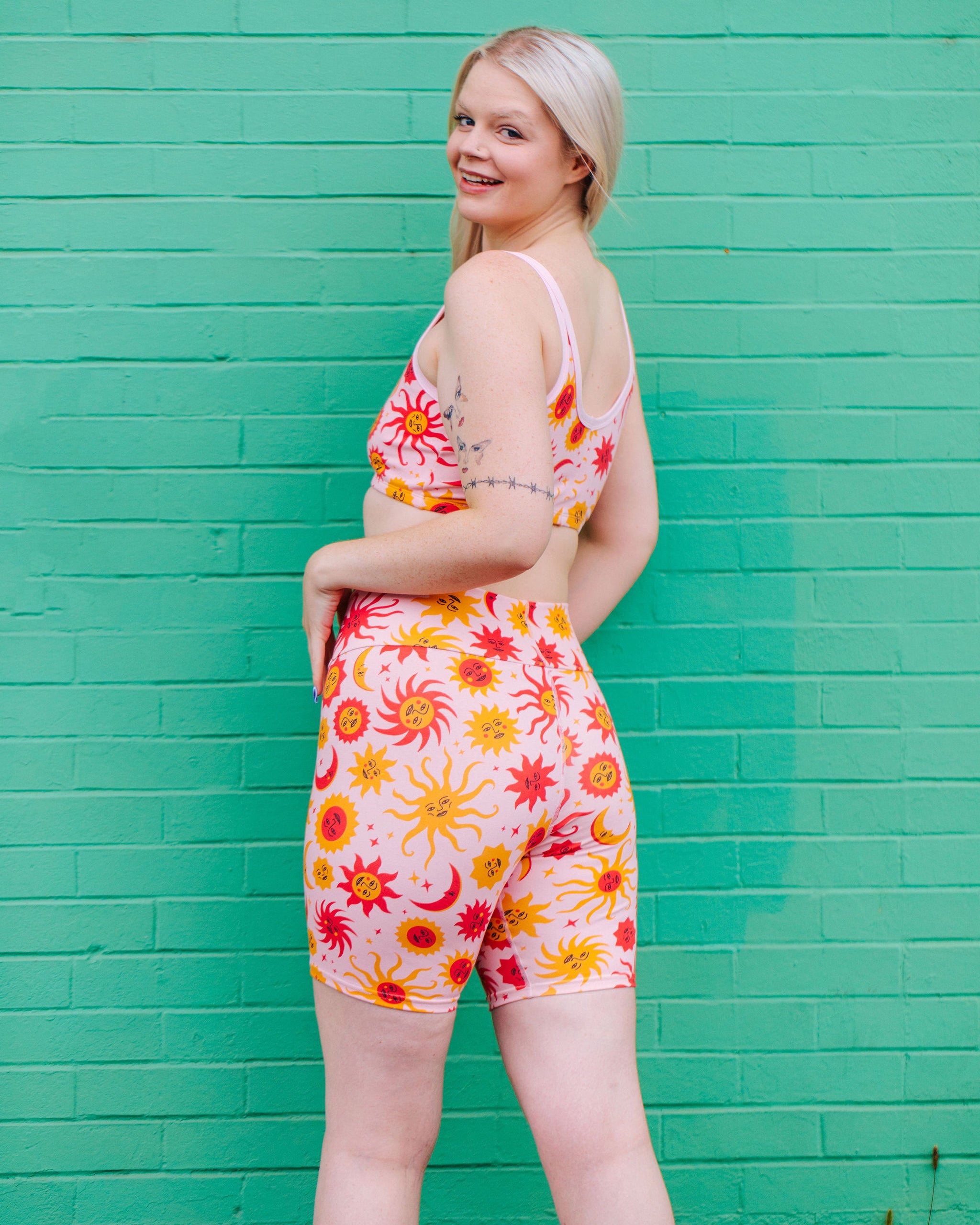 Model wearing Thunderpants Bike Shorts and Longline Bra in Luna y Sol print - pink, yellow, and orange suns and moons.