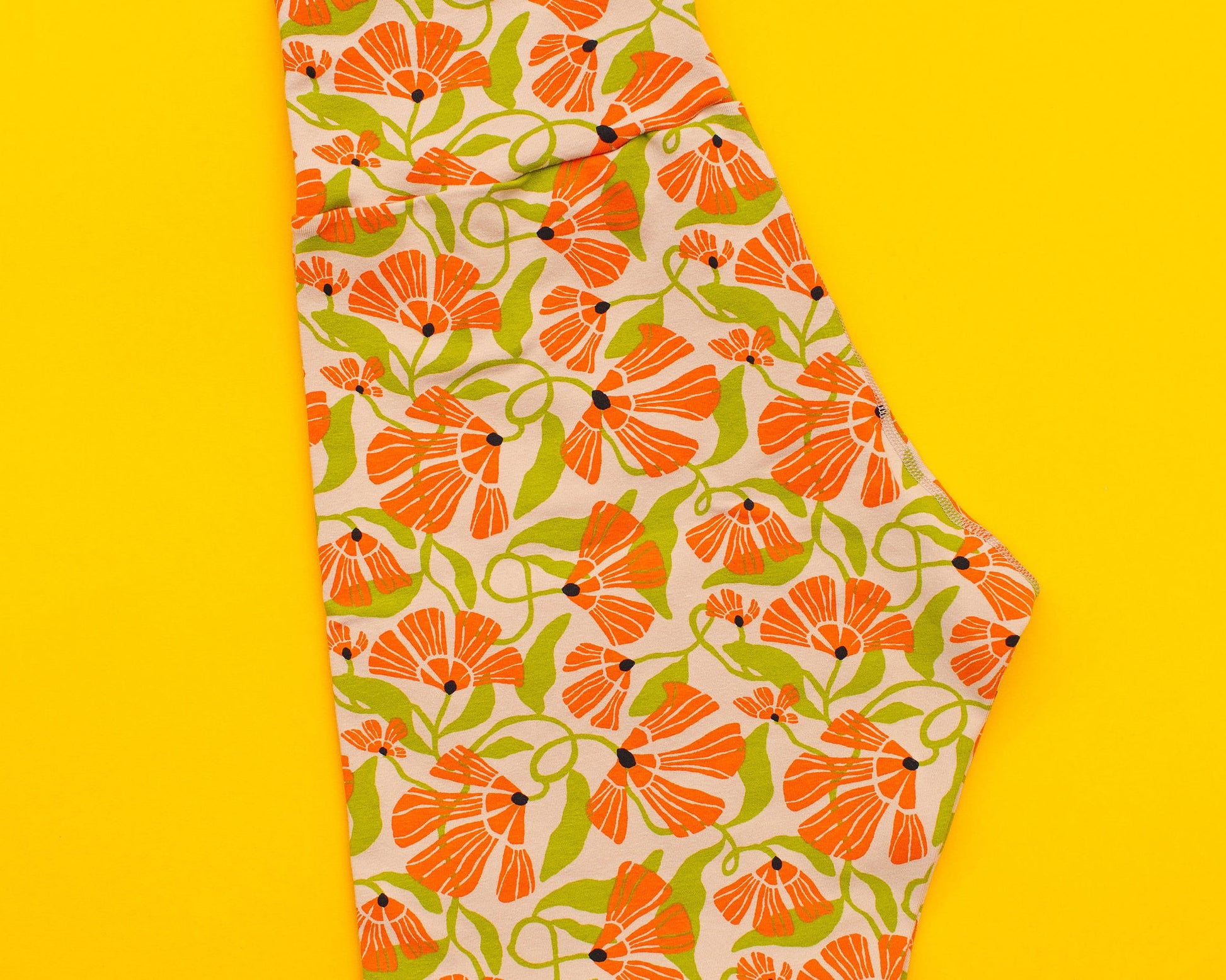 Flat lay of Thunderpants Bike Shorts in Secret Garden - tan background with orange and green flowers.