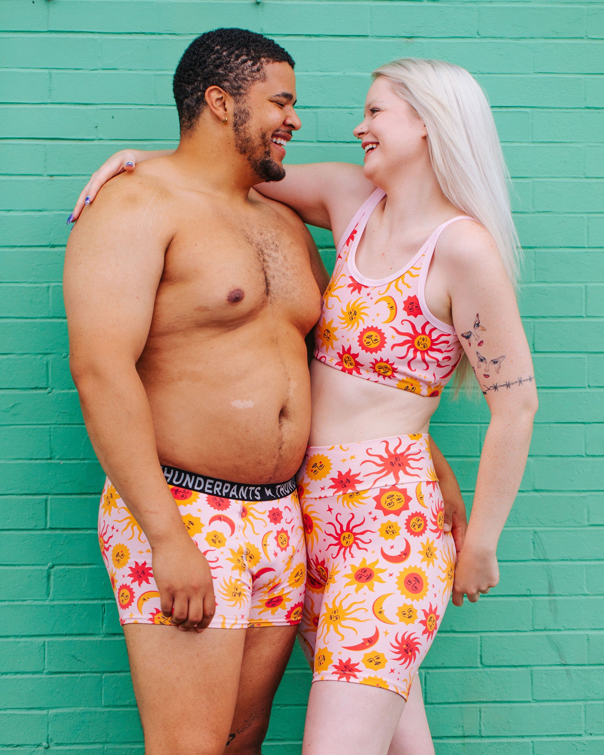 Two models wearing Thunderpants Bike Shorts, Longline Bra, and Boxer Brief style underwear in Luna y Sol print - pink, yellow, and orange suns and moons.