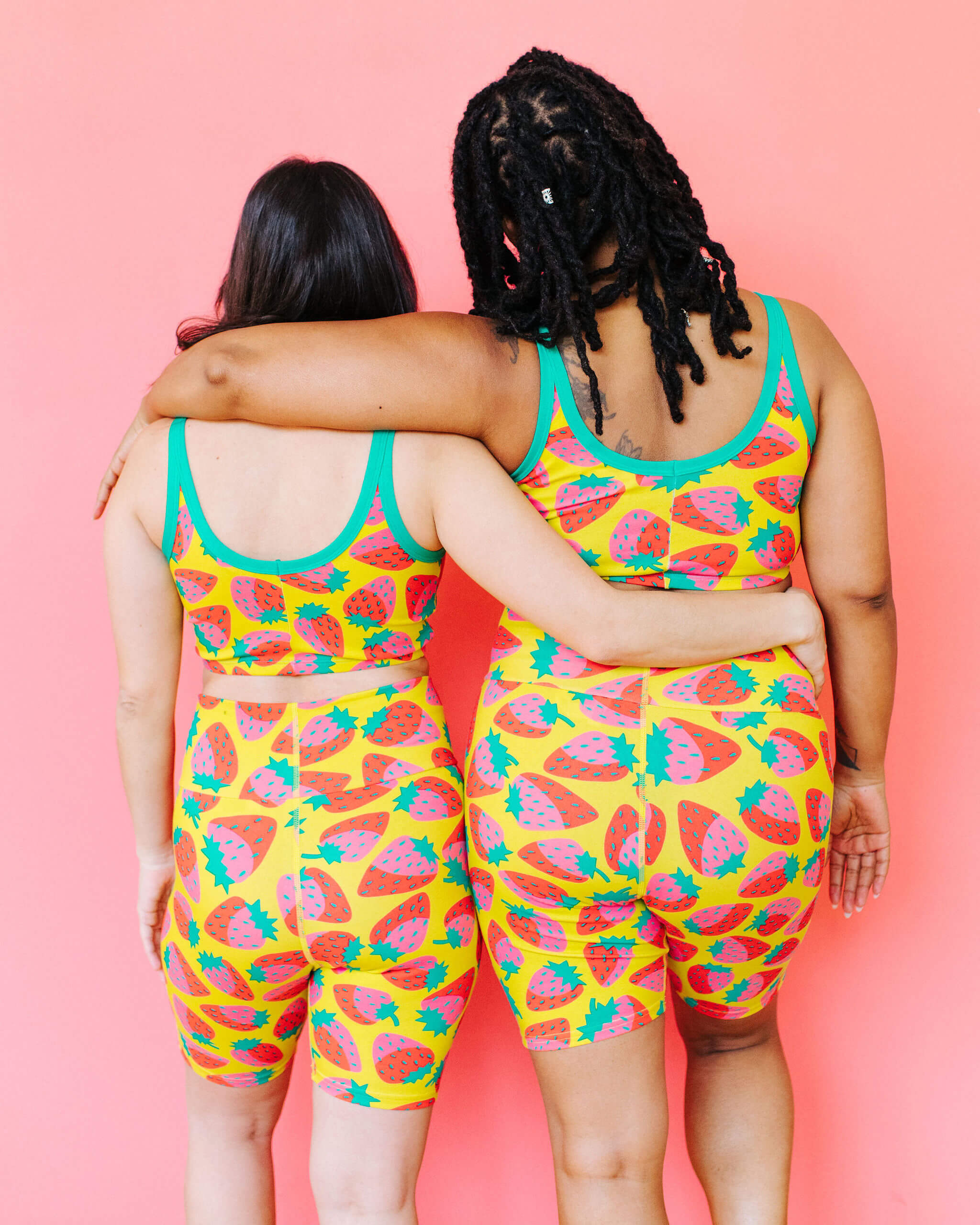 Models wearing Thunderpants Bike Shorts and Longline Bra in a Strawberry print - pink, red, and peacock green on chartreuse. 