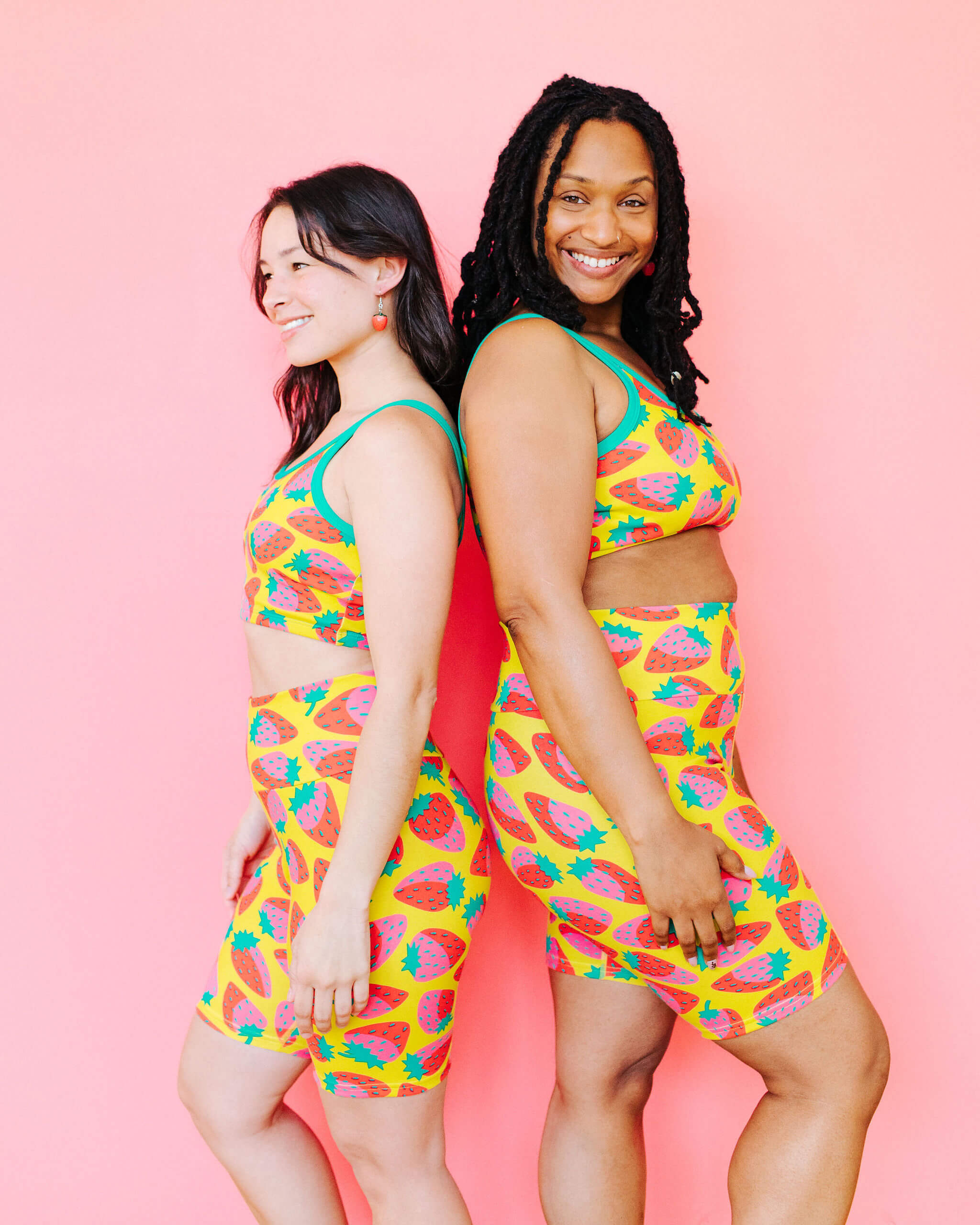 Models wearing Thunderpants Bike Shorts and Longline Bra in a Strawberry print - pink, red, and peacock green on chartreuse. 