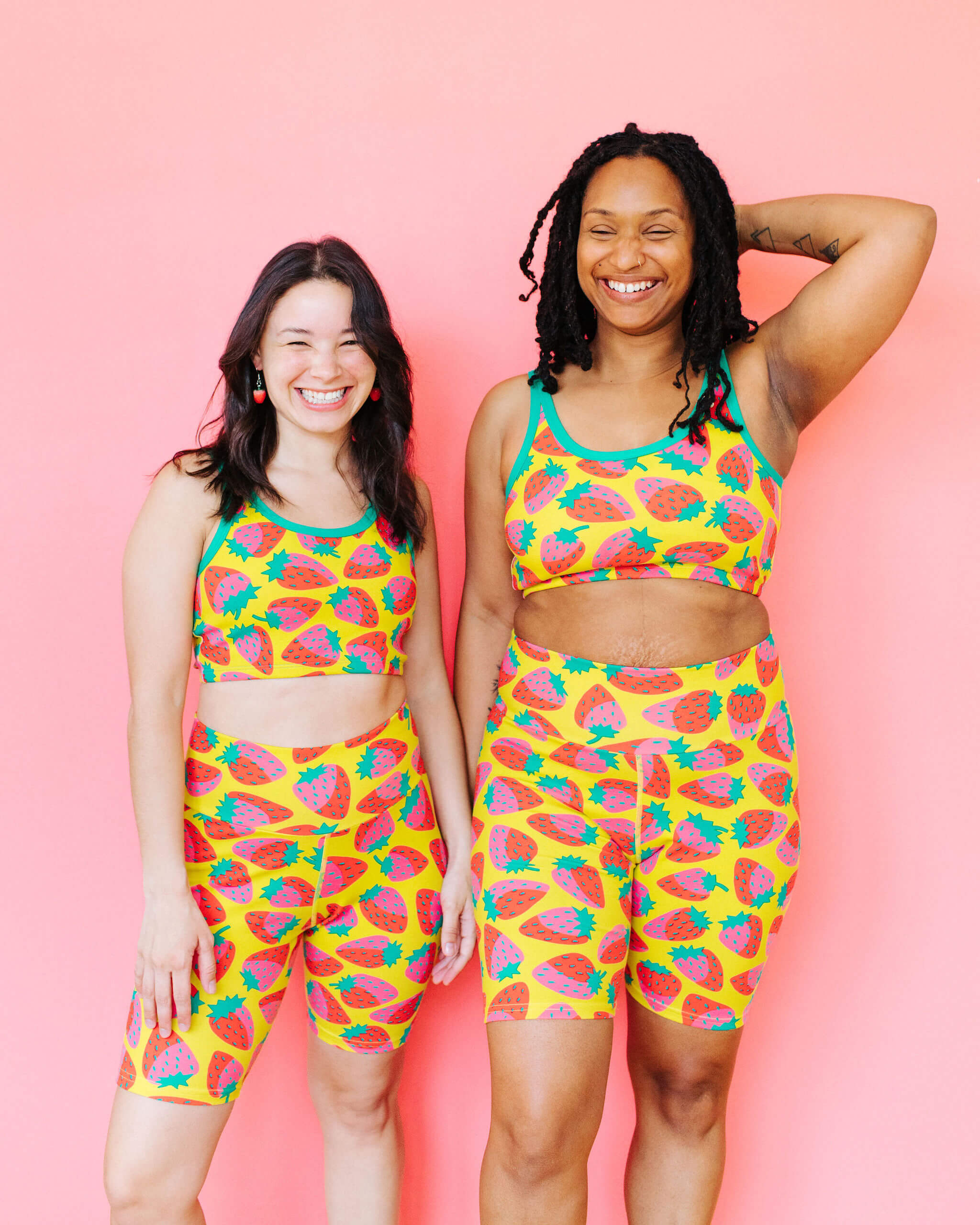 Models wearing Thunderpants Bike Shorts and Longline Bra in a Strawberry print - pink, red, and peacock green on chartreuse. 