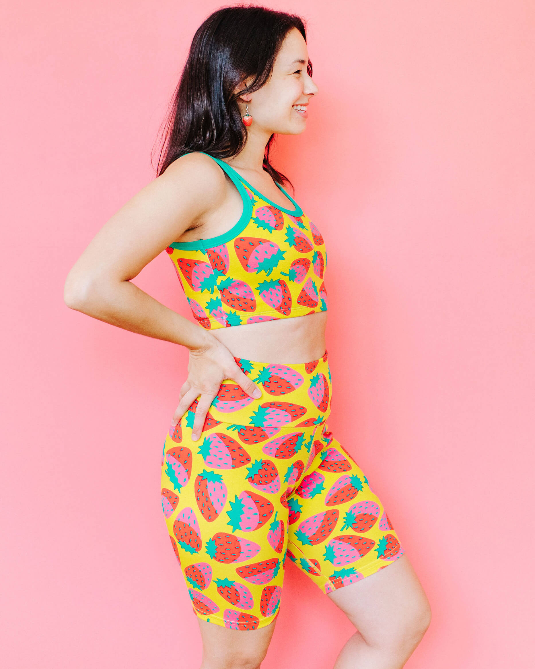 Model wearing Thunderpants Bike Shorts and Longline Bra in a Strawberry print - pink, red, and peacock green on chartreuse. 