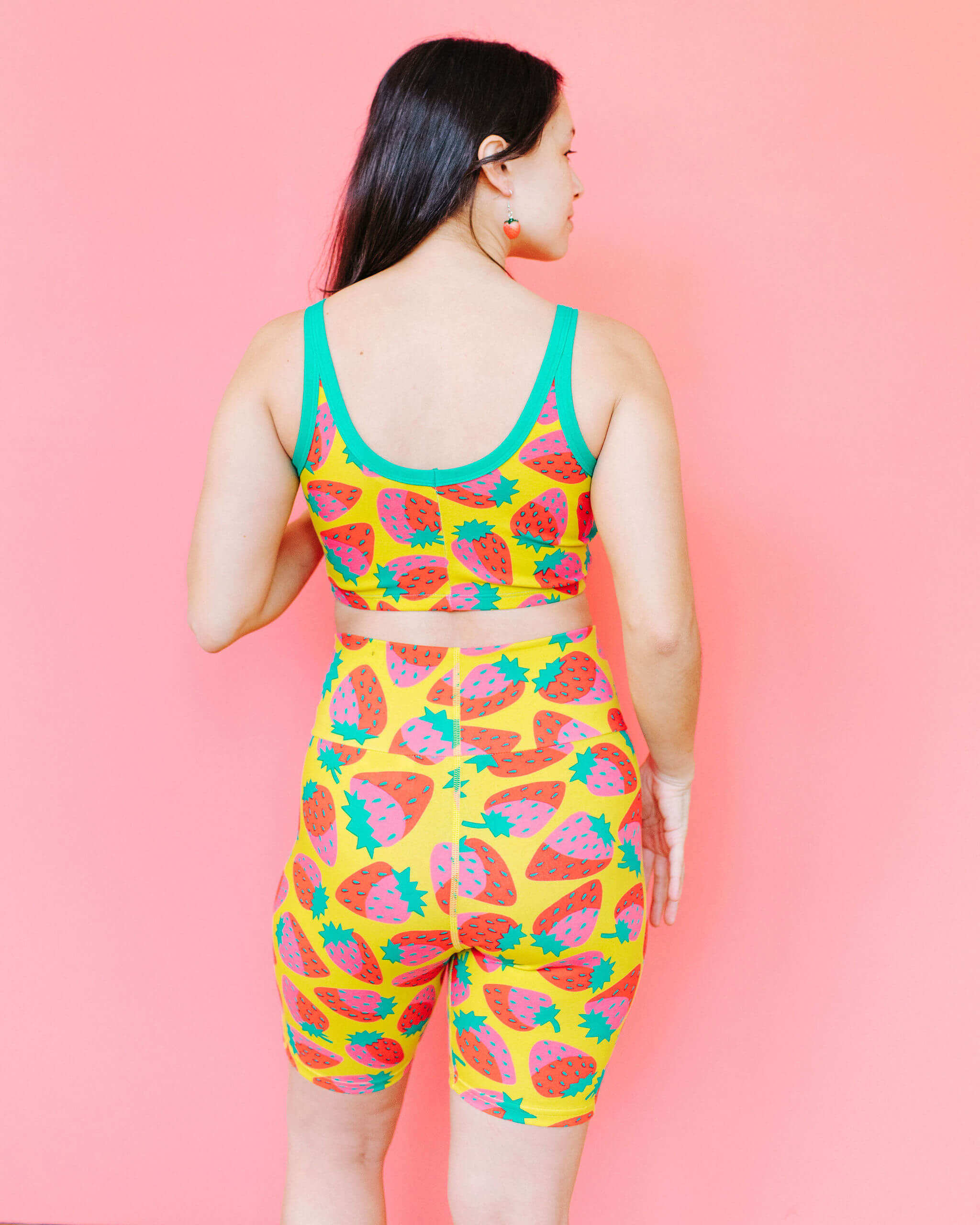 Model wearing Thunderpants Bike Shorts and Longline Bra in a Strawberry print - pink, red, and peacock green on chartreuse. 