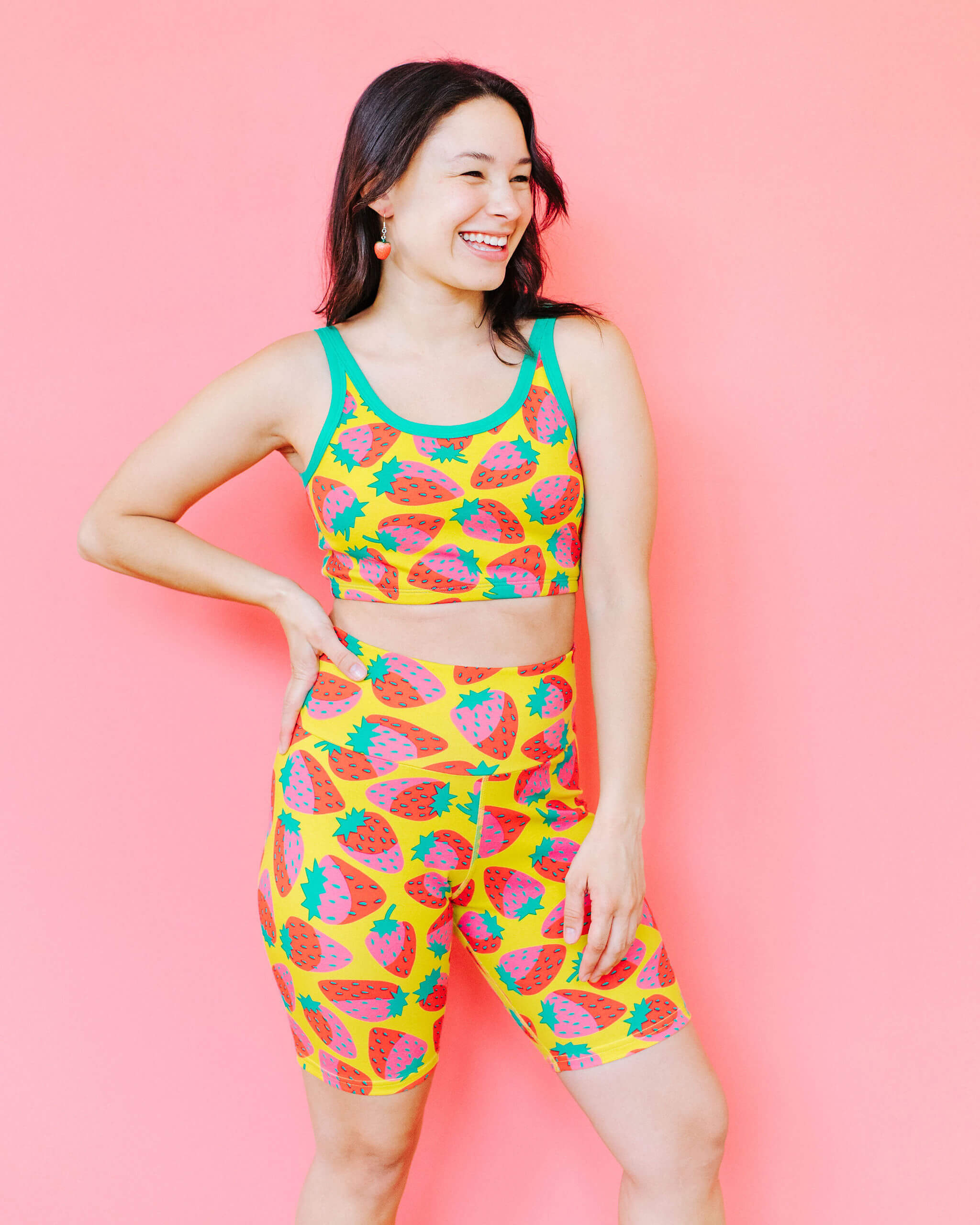 Model wearing Thunderpants Bike Shorts and Longline Bra in a Strawberry print - pink, red, and peacock green on chartreuse. 
