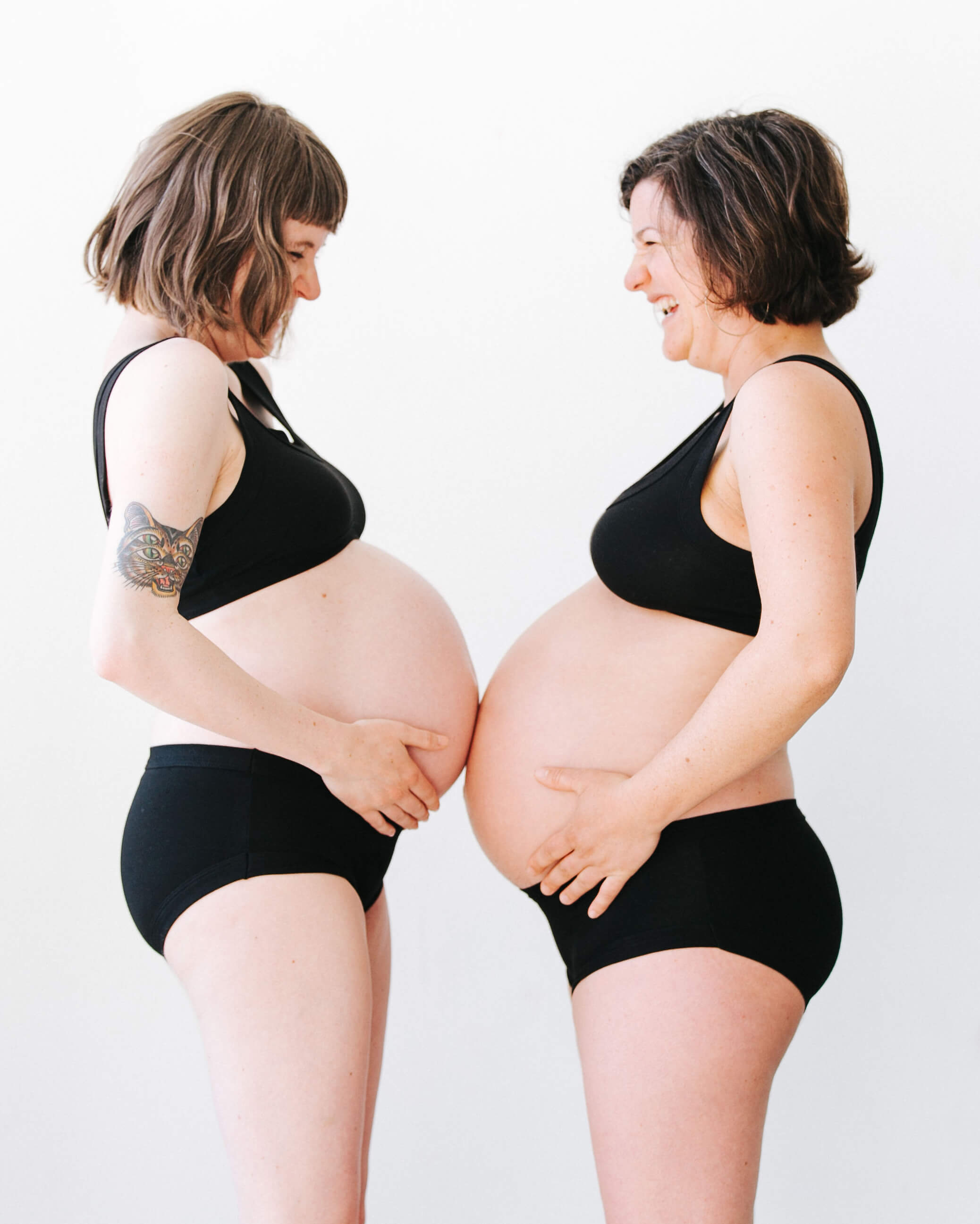 Two pregnant models wearing a set of Thunderpants Hipster style underwear and Bralette in Plain Black.