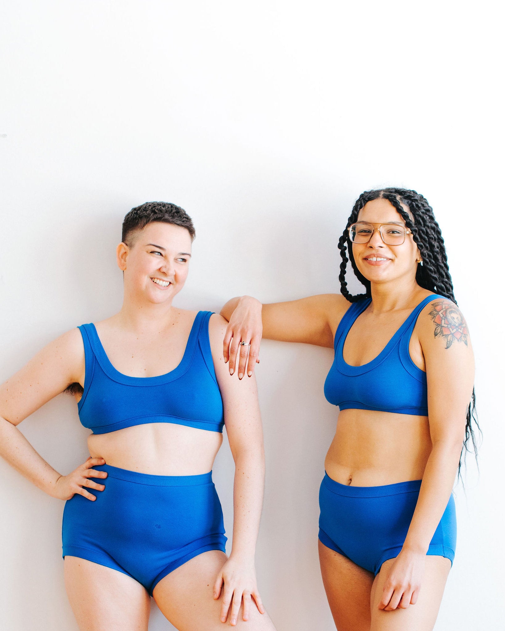 Two models smiling together wearing Thunderpants Bralette and underwear sets in Blueberry Blue.