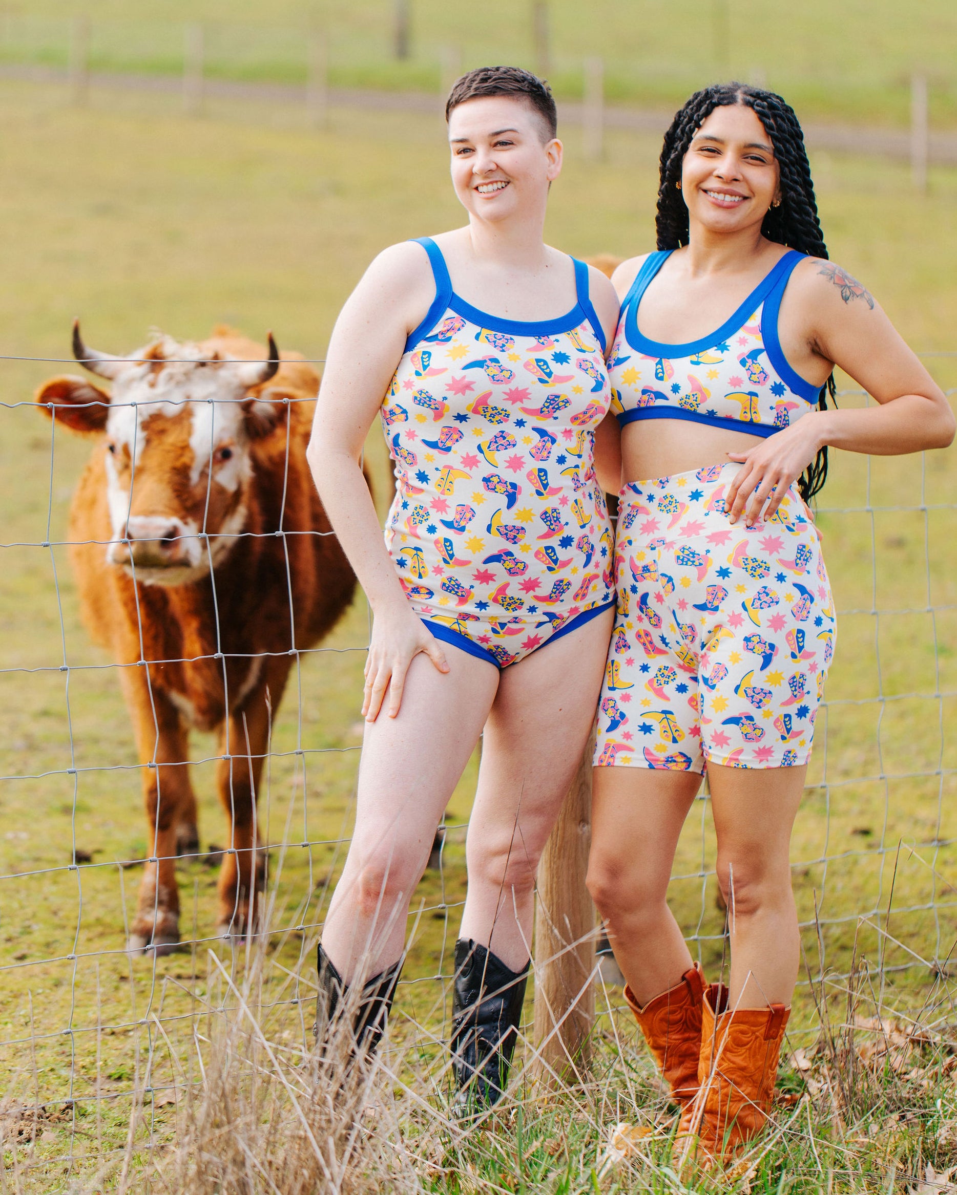 Two models in a field with a cow wearing various Thunderpants sets in Boot Scootin' - fun boots in pink, yellow, and blue.
