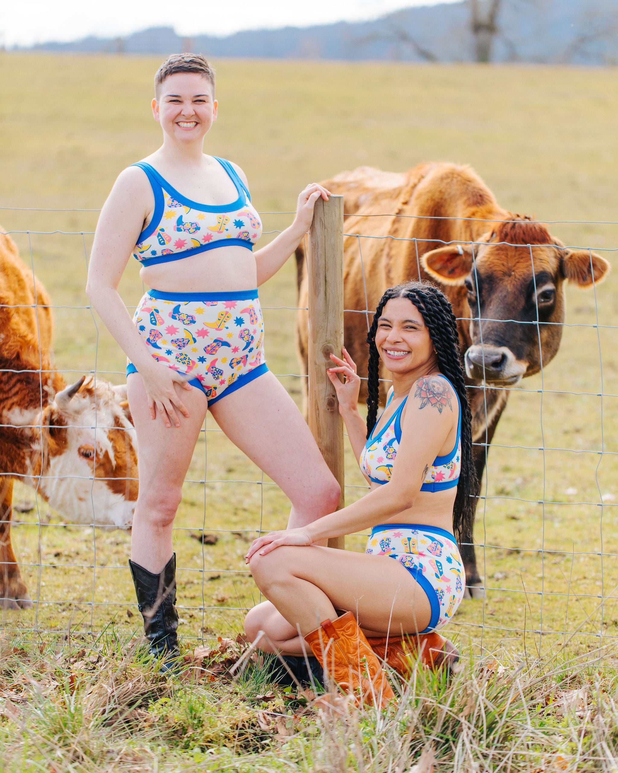 Two models in a field with cows in Thunderpants sets in Boot Scootin' - fun boots in pink, yellow, and blue.