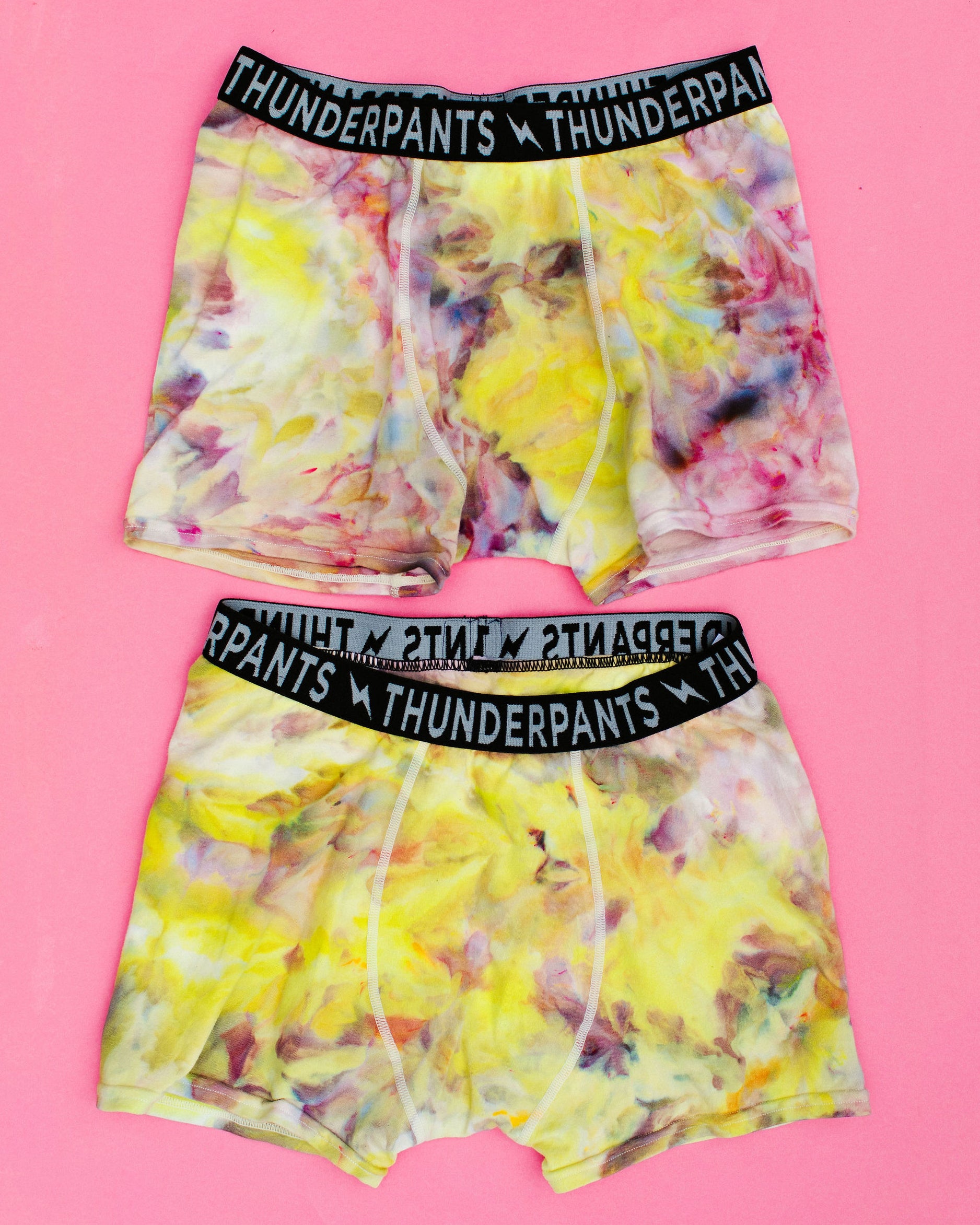 Flat lay of two Thunderpants Boxer Brief style underwear in Citrus Blossom Dye - hand dyed yellow, pink, and purple.