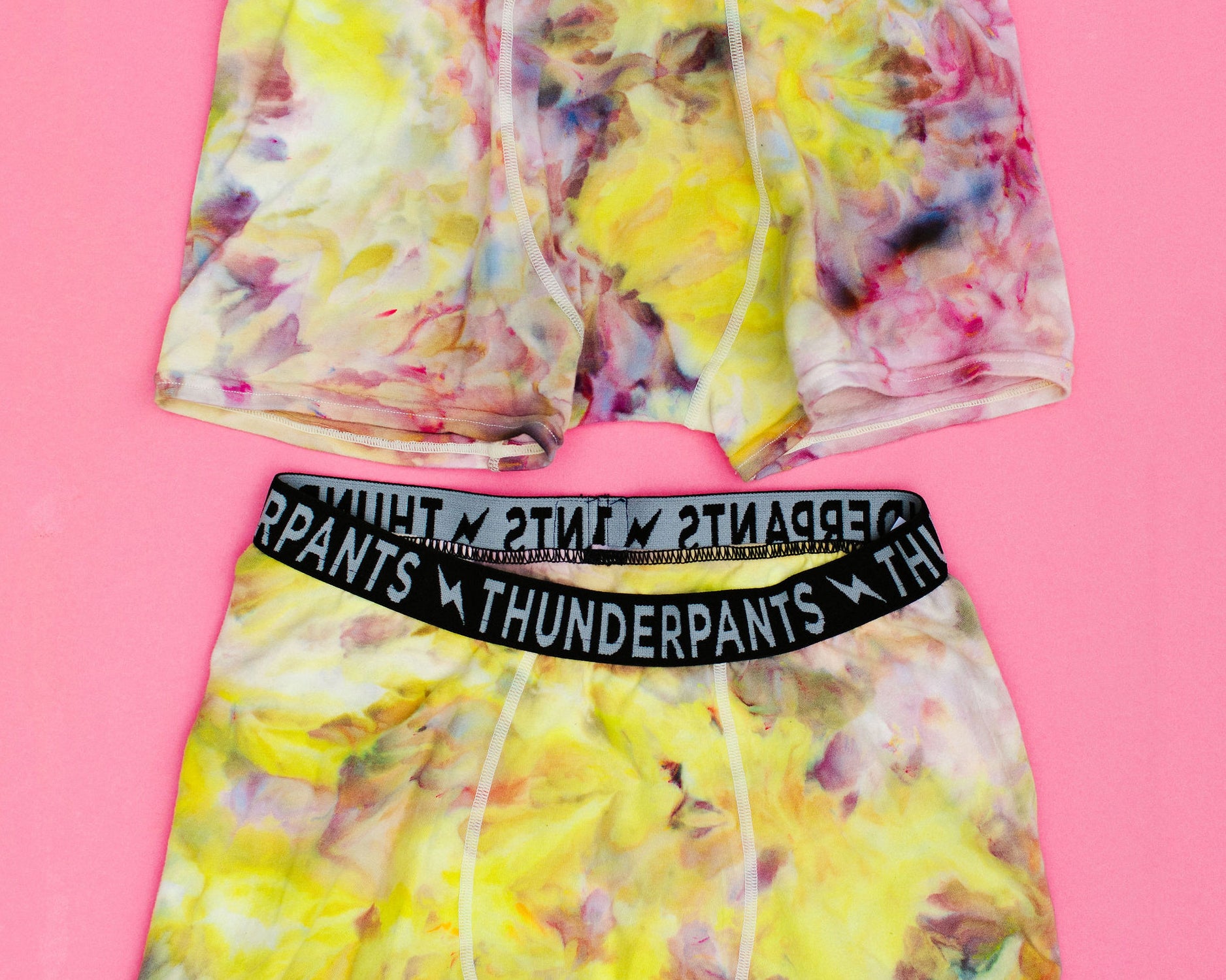 Flat lay of two Thunderpants Boxer Brief style underwear in Citrus Blossom Dye - hand dyed yellow, pink, and purple.