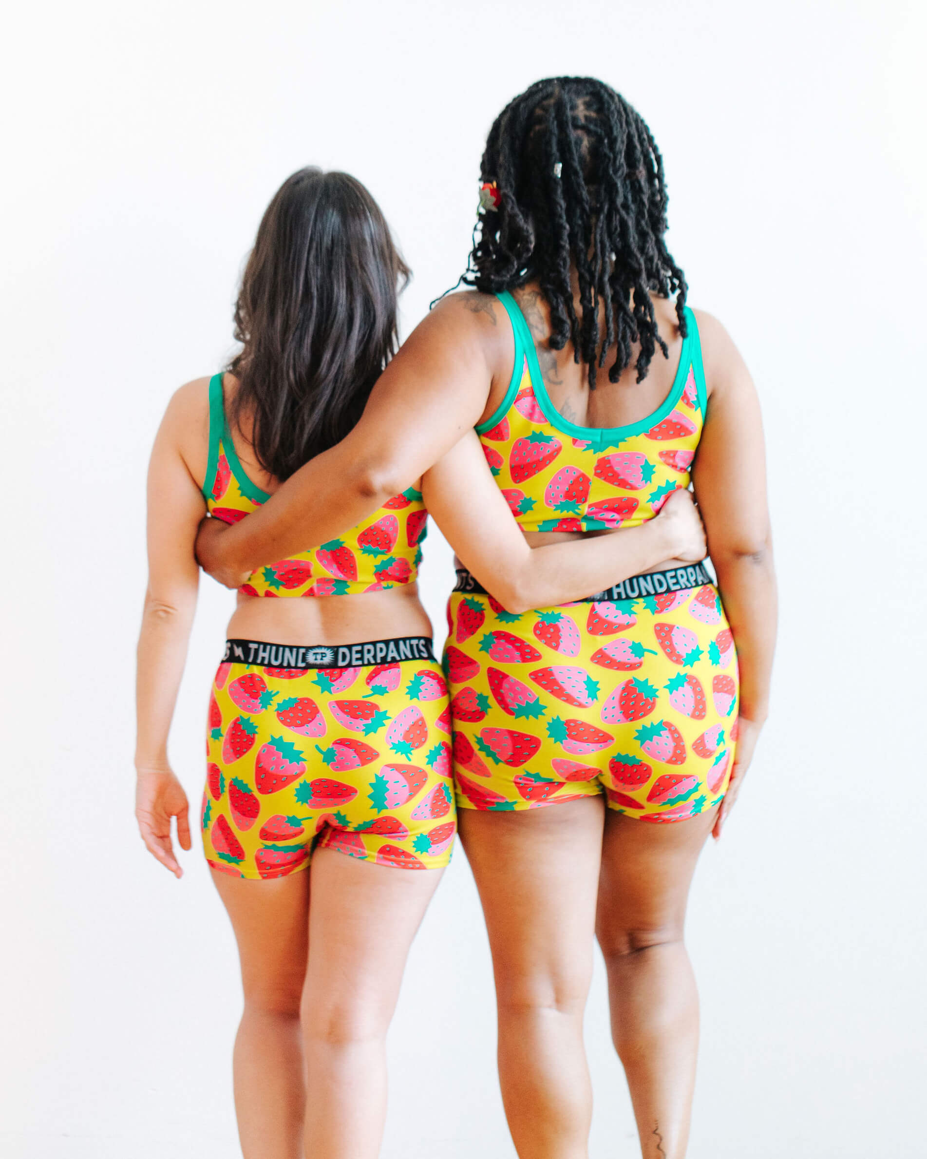 Models wearing Thunderpants Boxer Brief and Longline Bra in a Strawberry print - pink, red, and peacock green on chartreuse. 