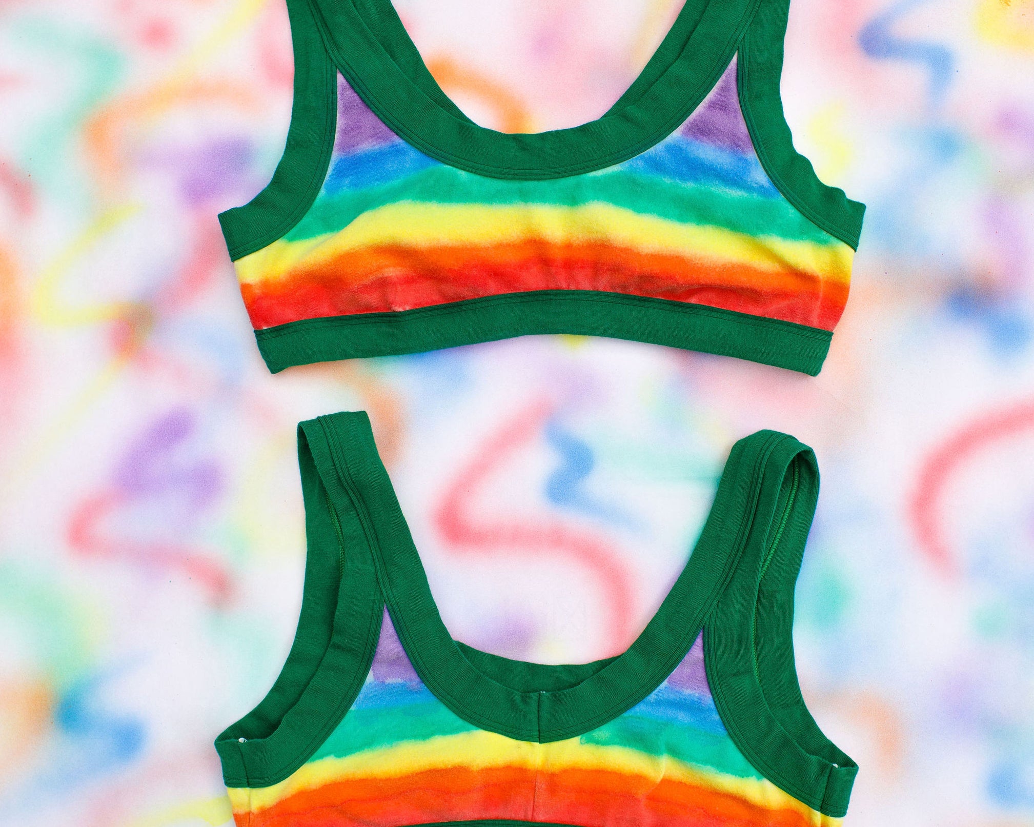 Flat lay of two Thunderpants Bralettes in rainbow dye with emerald green binding.