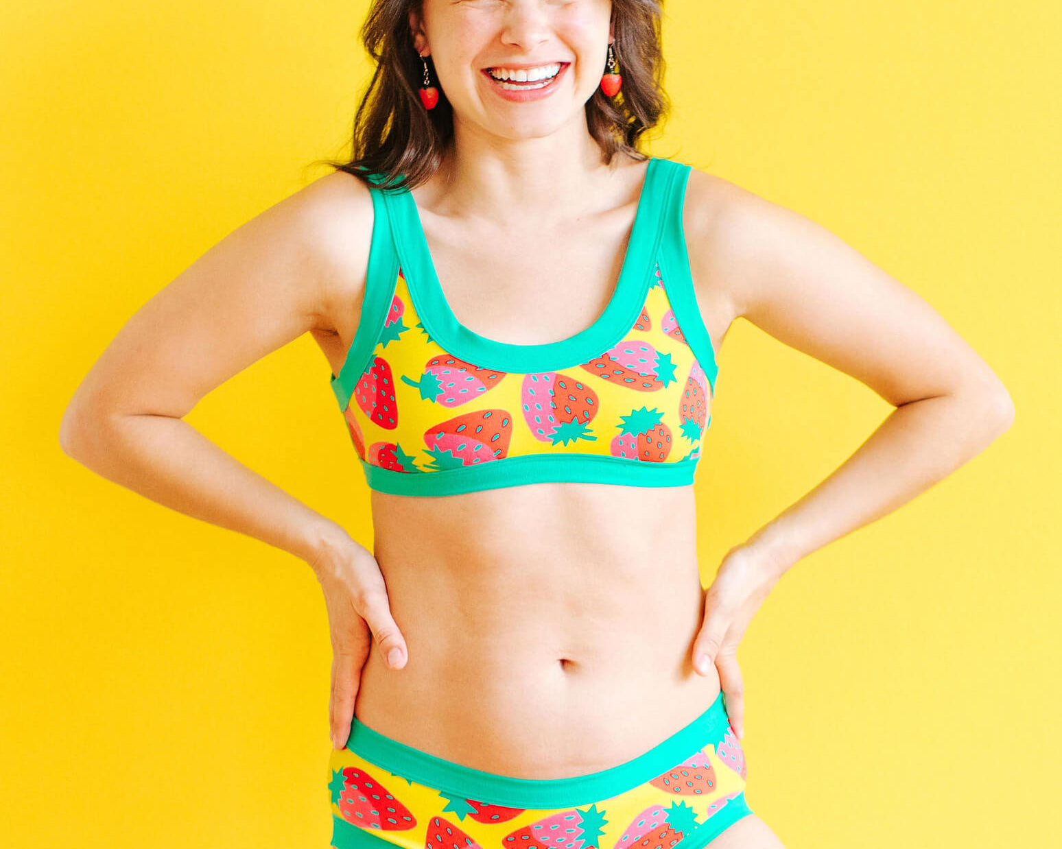Model wearing Thunderpants Bralette and Hipster style underwear in a Strawberry print - pink, red, and peacock green on chartreuse. 