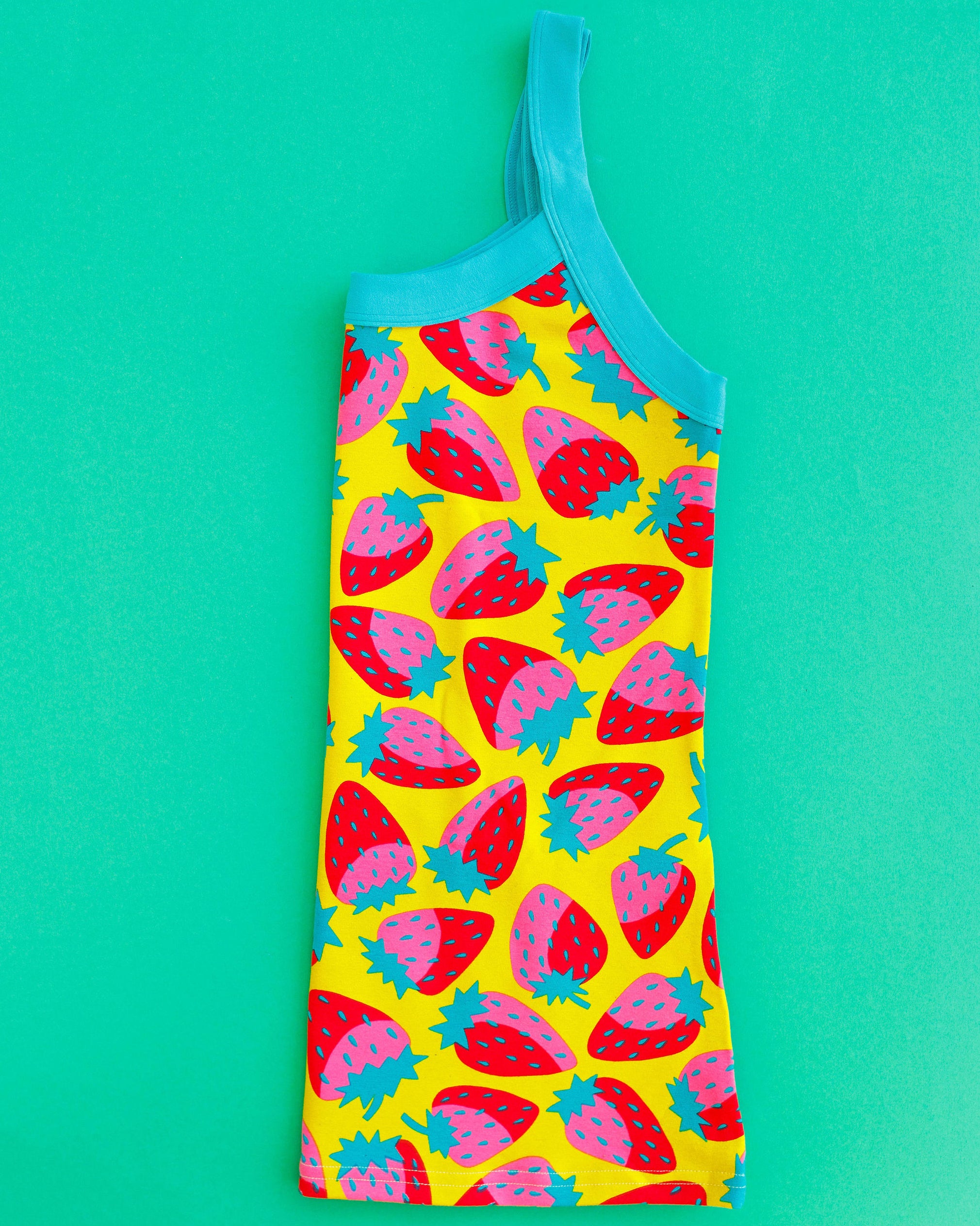 Flat lay of folded Thunderpants Cami in Strictly Strawberry - pink, red, and green strawberry on a yellow background.