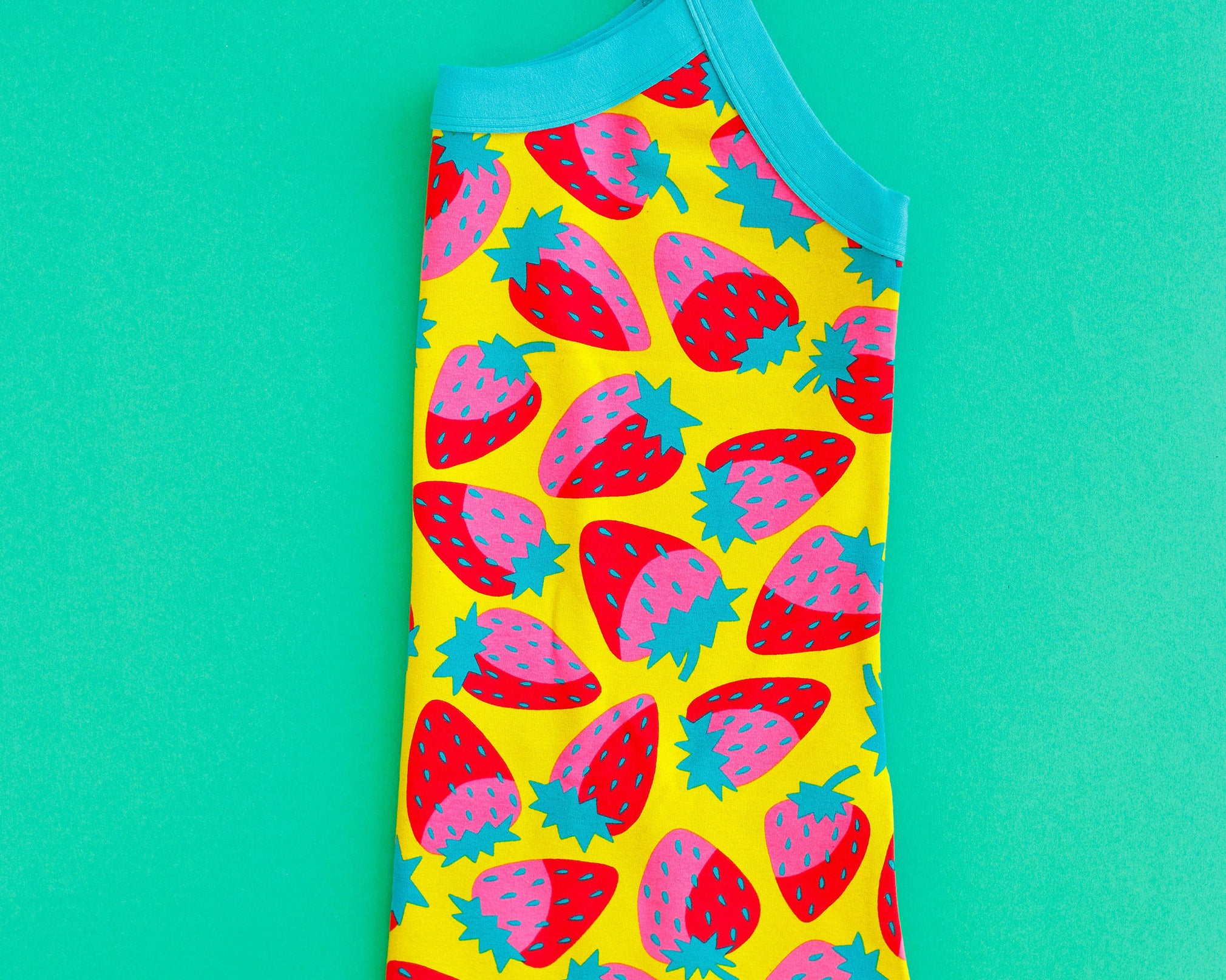 Flat lay of folded Thunderpants Cami in Strictly Strawberry - pink, red, and green strawberry on a yellow background.