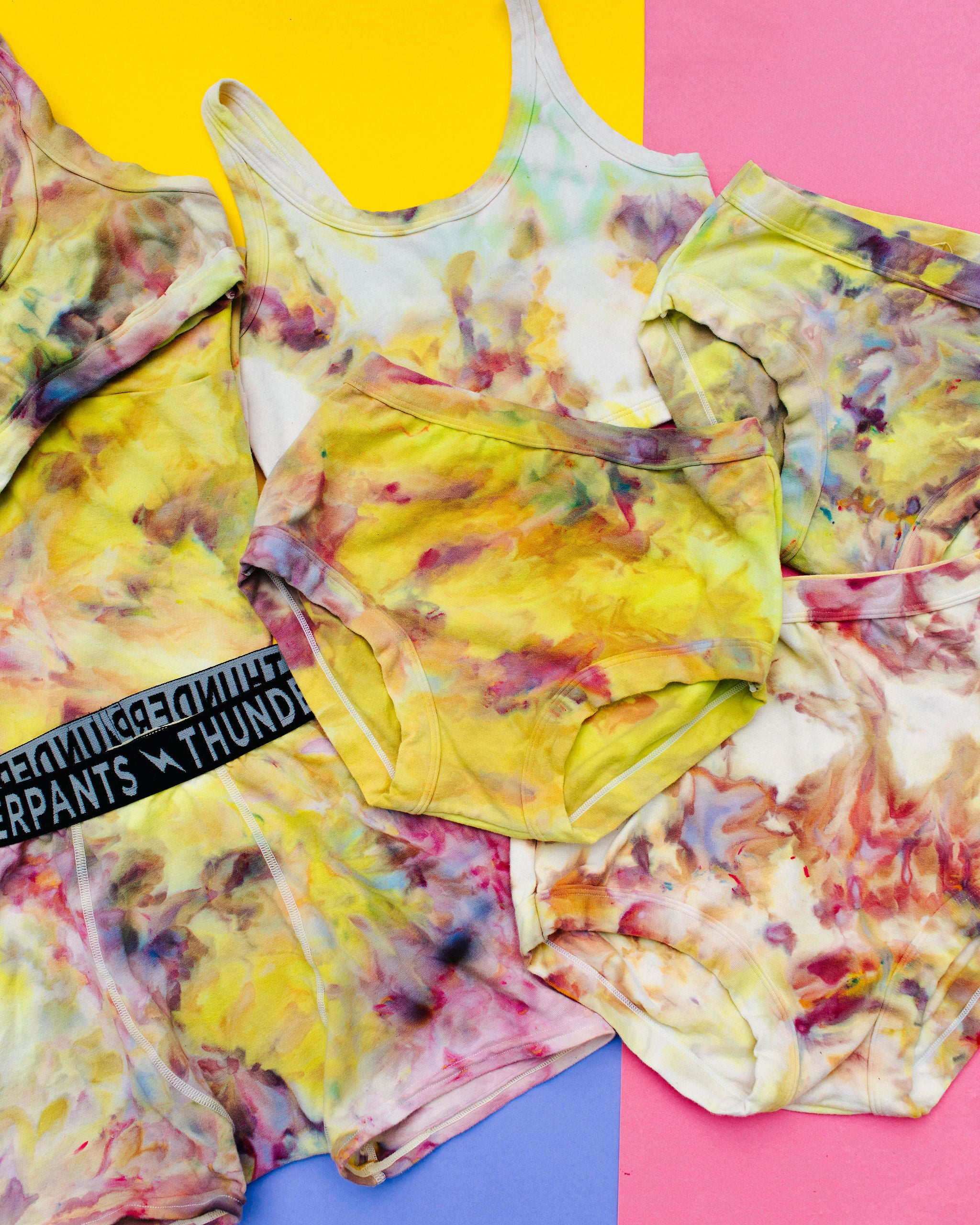 Flat lay of multiple Thunderpants styles in Citrus Blossom Dye - hand dyed yellow, pink, and purple.