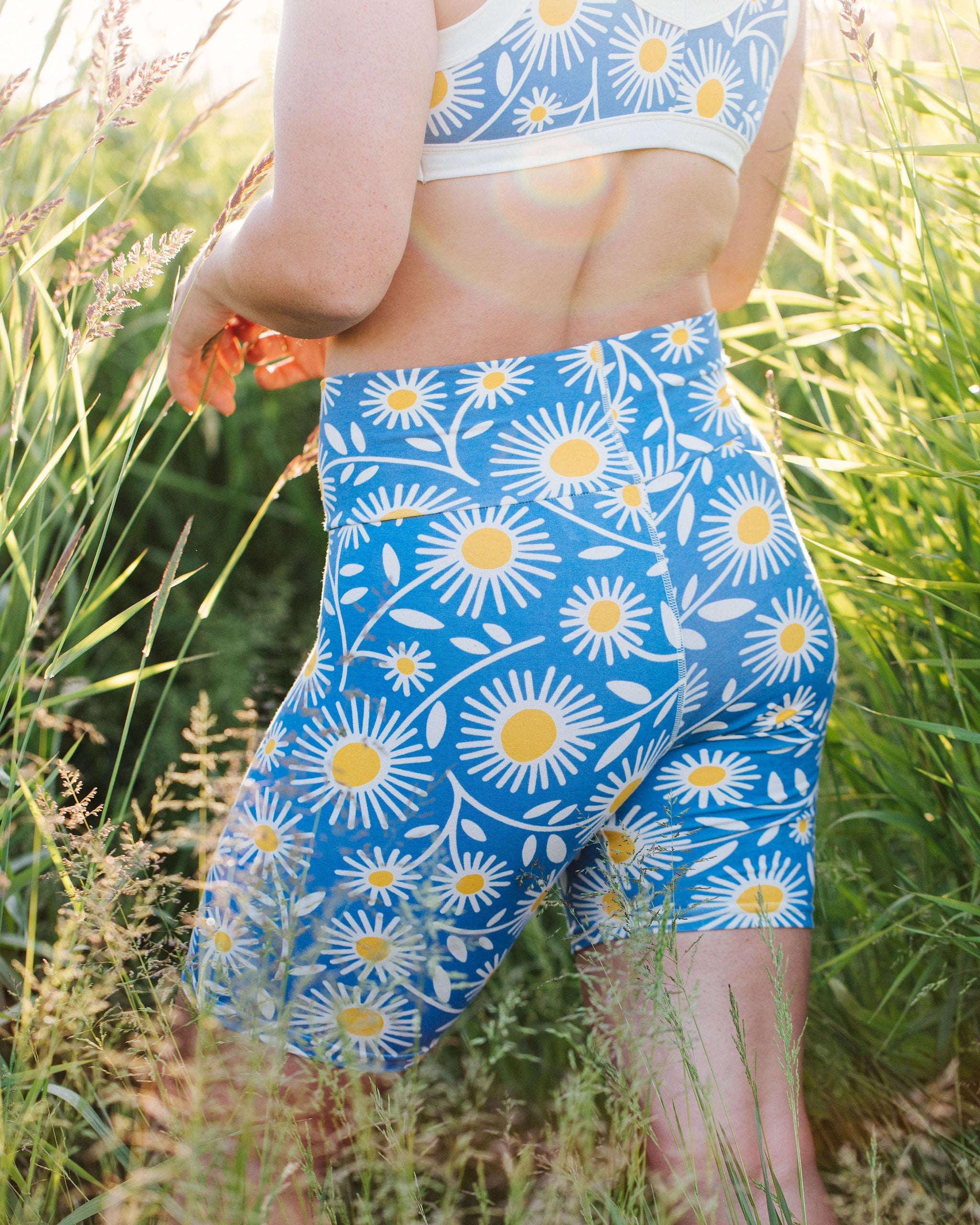 Close up of model in a field wearing Thunderpants Bike Shorts in Daisy Days print: blue with white and yellow daisies.