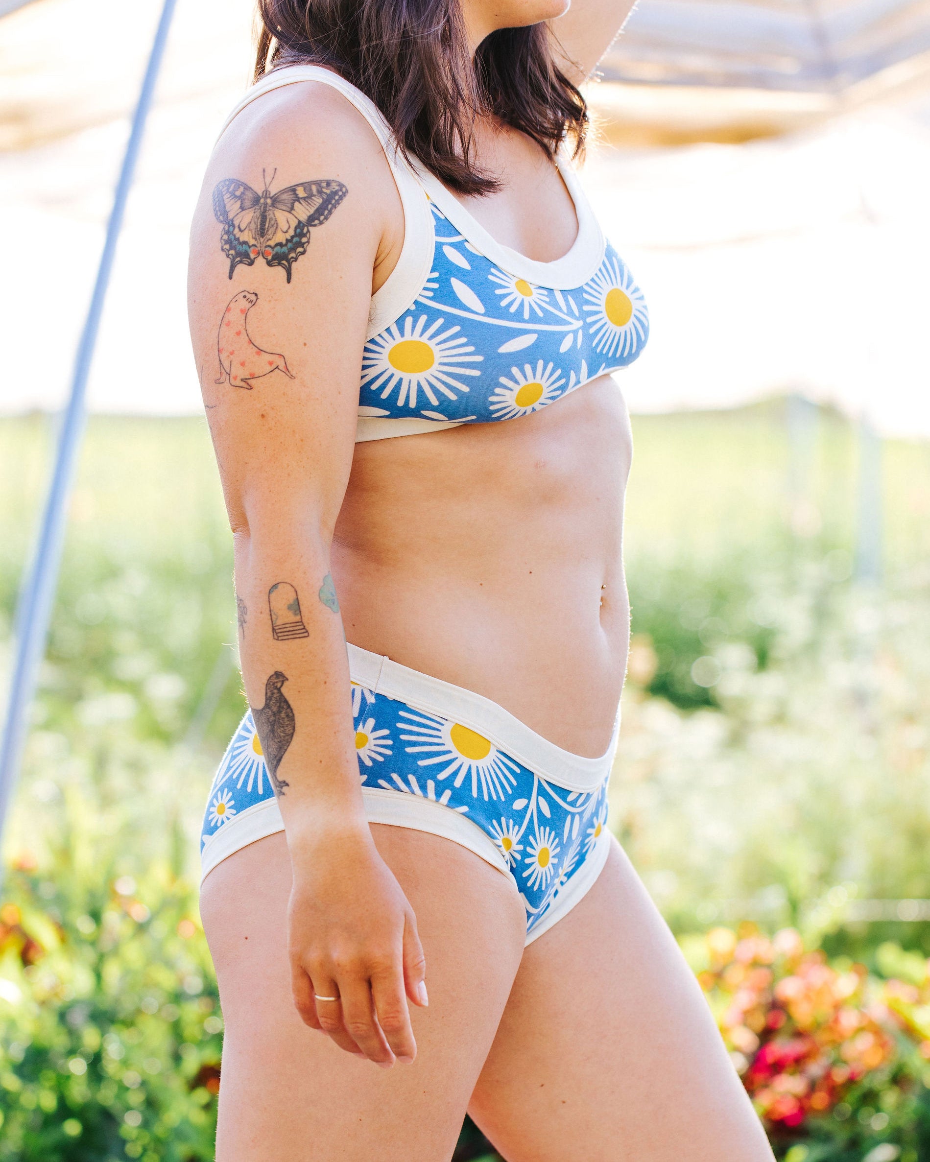 Close up of model standing in a field wearing Thunderpants Hipster style underwear and Bralette in Daisy Days print: blue with white and yellow daisies.