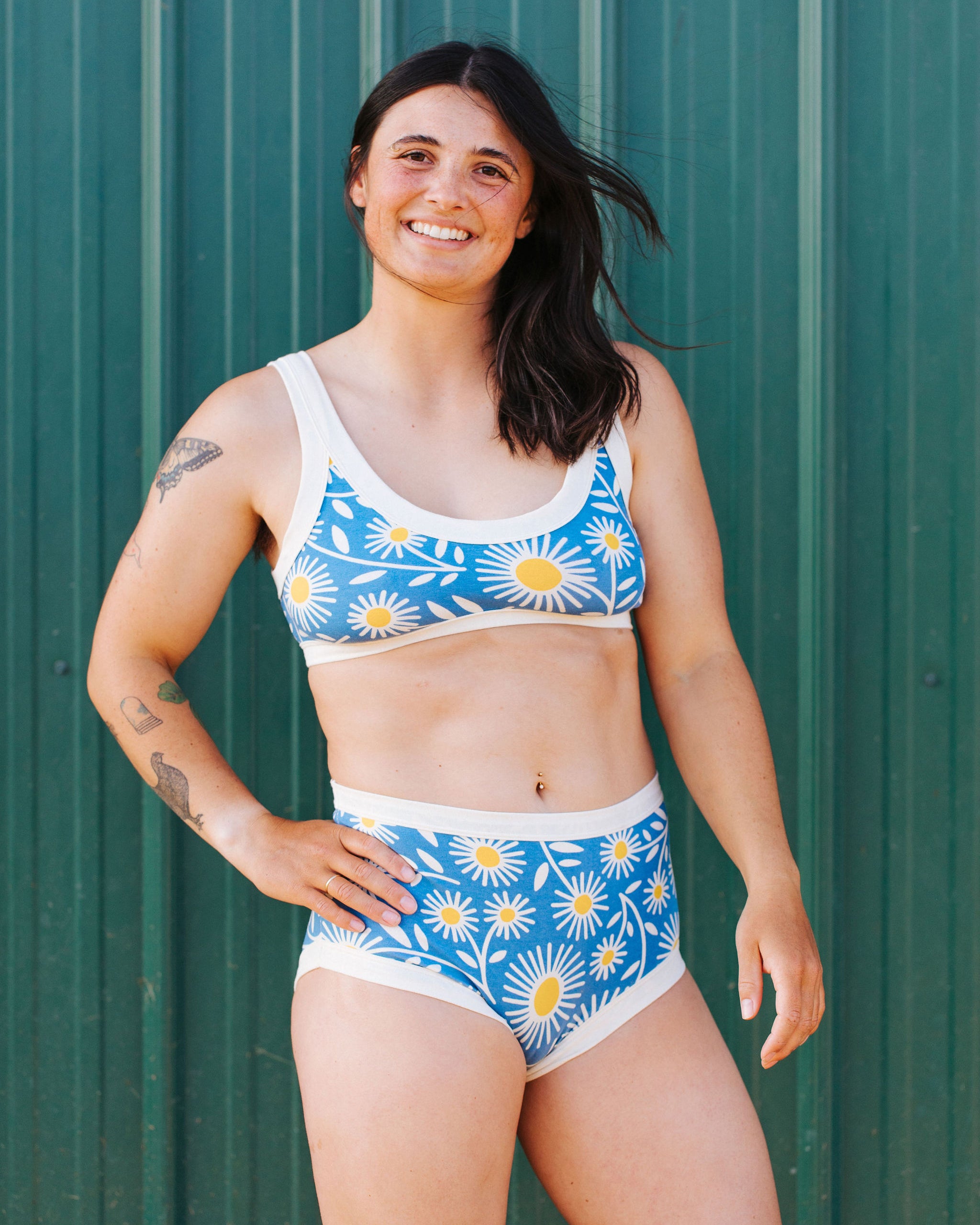 Model in front of a green wall wearing Thunderpants Original style underwear and Bralette in Daisy Days print: blue with white and yellow daisies.