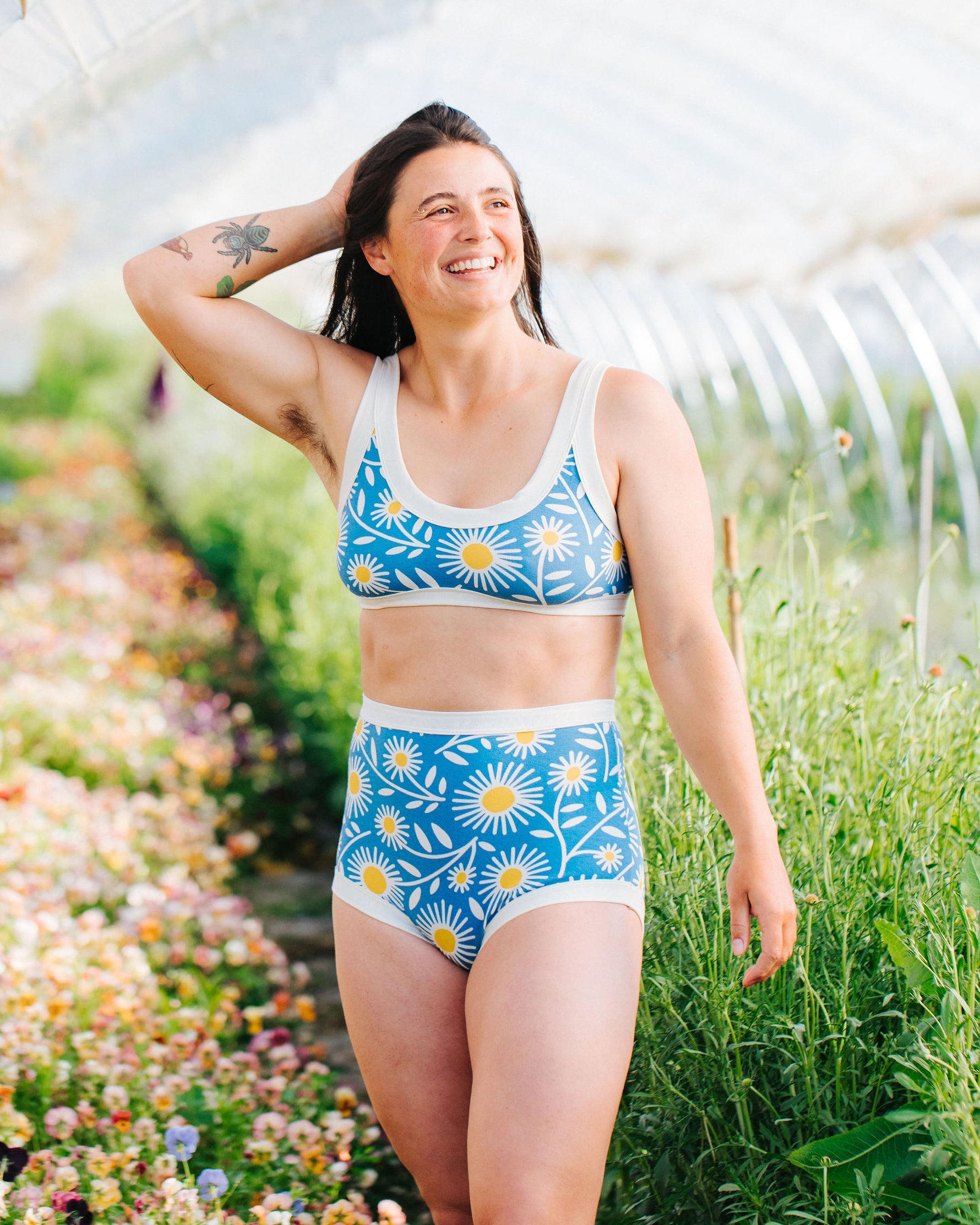 Model is smiling in a field wearing Thunderpants Sky Rise style underwear and a Bralette in Daisy Days print: blue with white and yellow daisies.