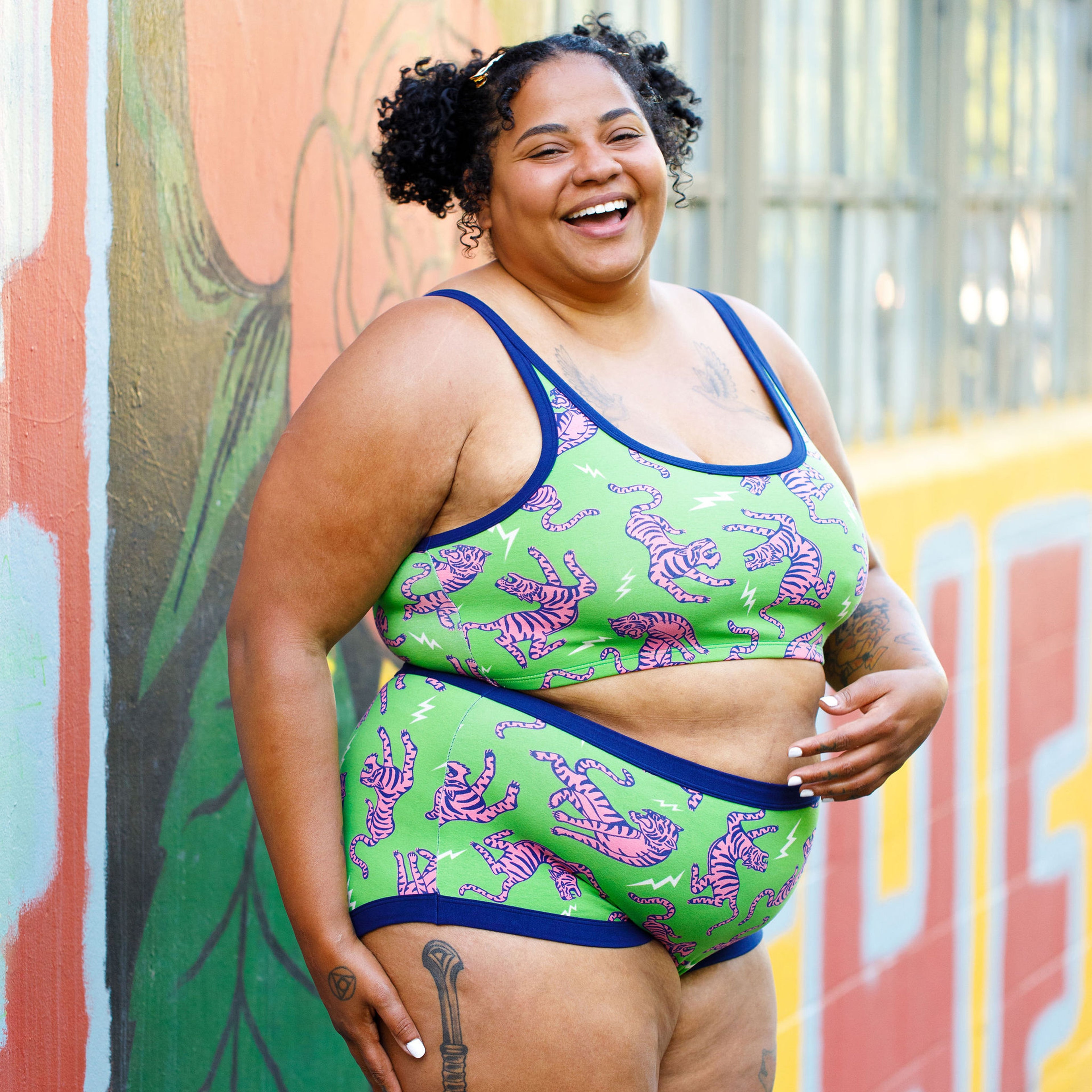Model wearing a set of organic cotton Thunderpants Electric Tiger print - pink and blue tigers on a green background.