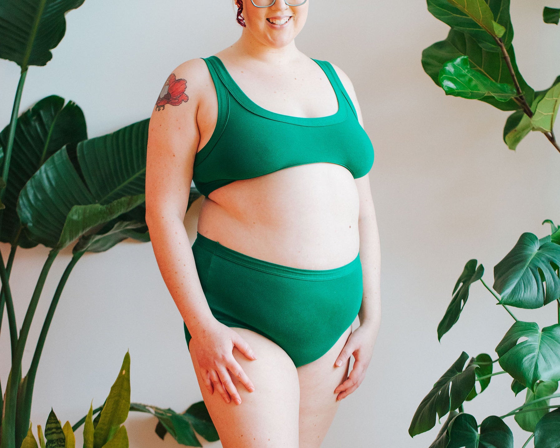 Model smiling in front of a bunch of plants wearing a Bralette and Original style underwear in Emerald Green.