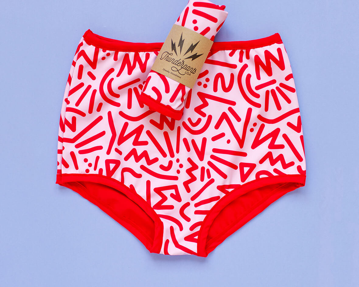 Flat lay of Thunderpants Sky Rise style Swim Bottoms in Energy Vibe print: light pink with dark pink designs.