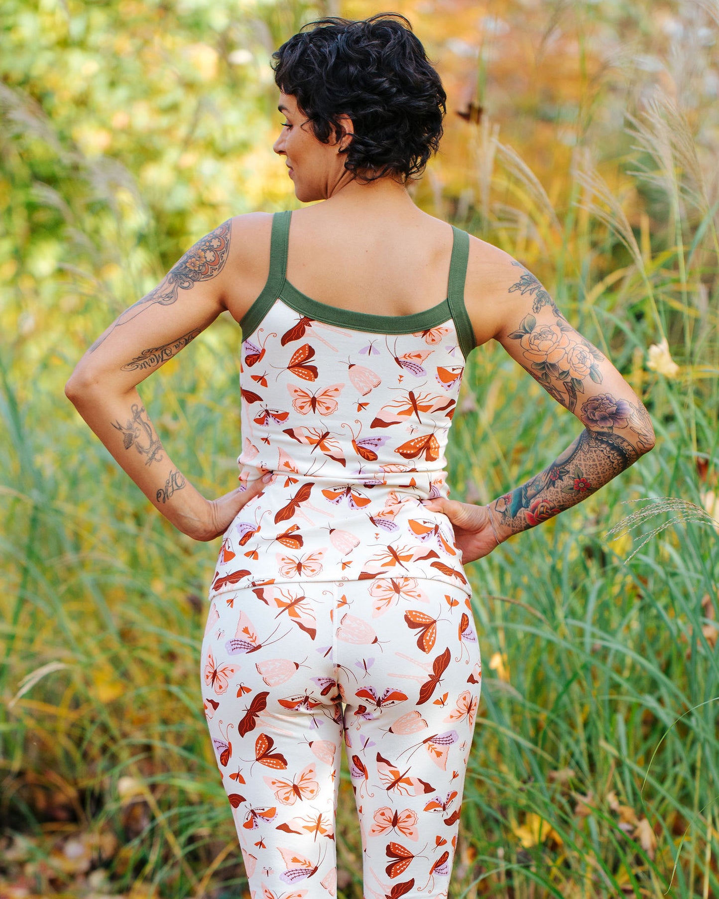 A model wearing Thunderpants Cami and Leggings in Field Study: a moth print in red, orange, pink, and purple bound in green.