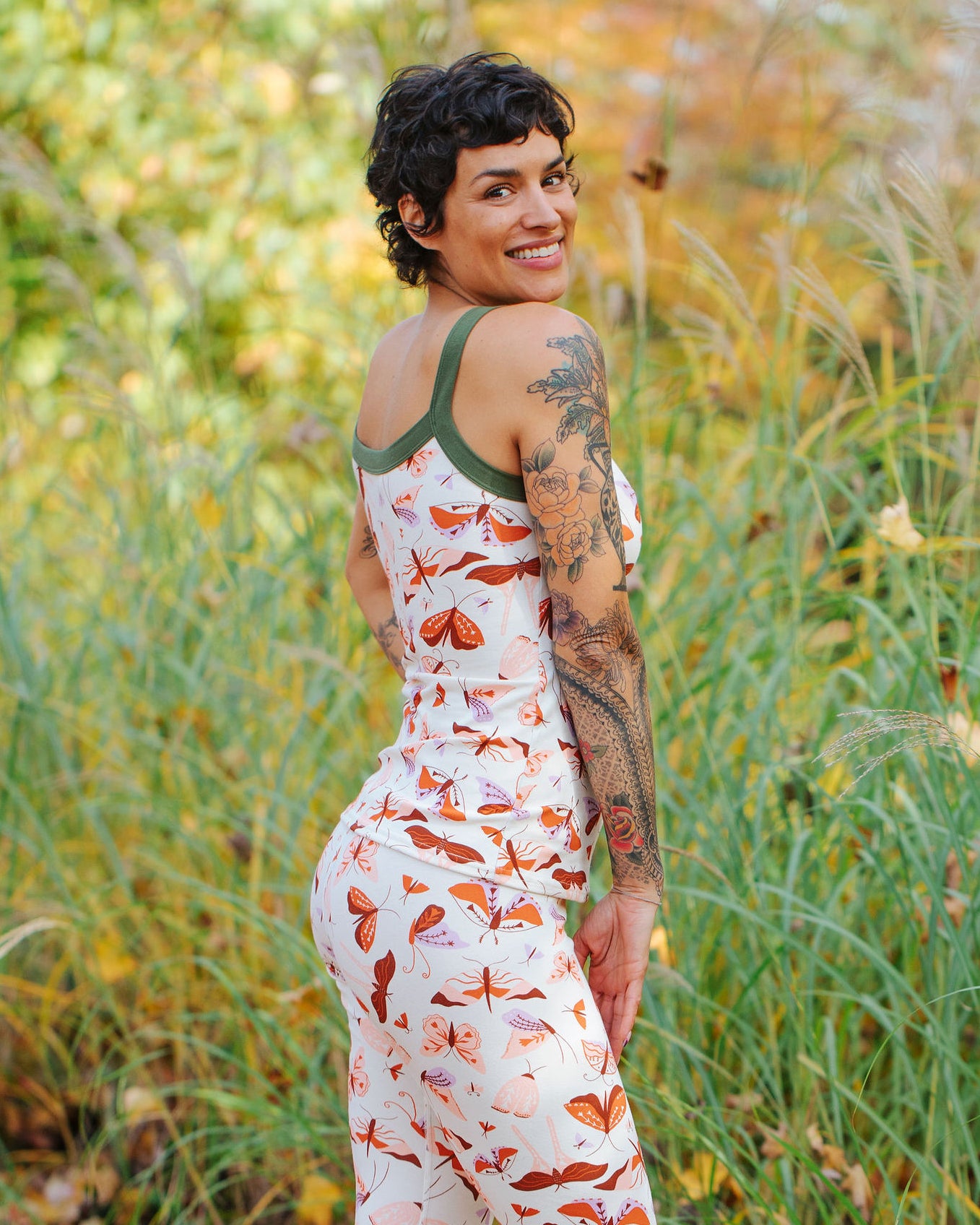 A model wearing Thunderpants Cami and Leggings in Field Study: a moth print in red, orange, pink, and purple bound in green.