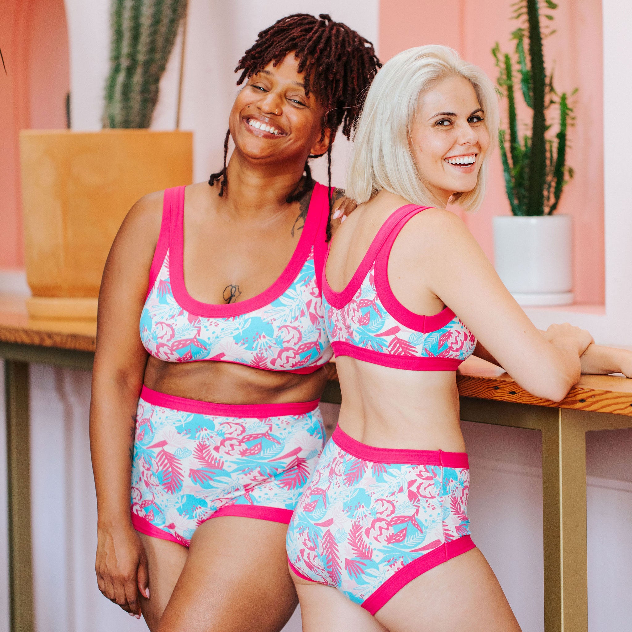 Two models smiling while wearing different styles of Thunderpants in Finding Flamingos print - pink and blue Miami style.