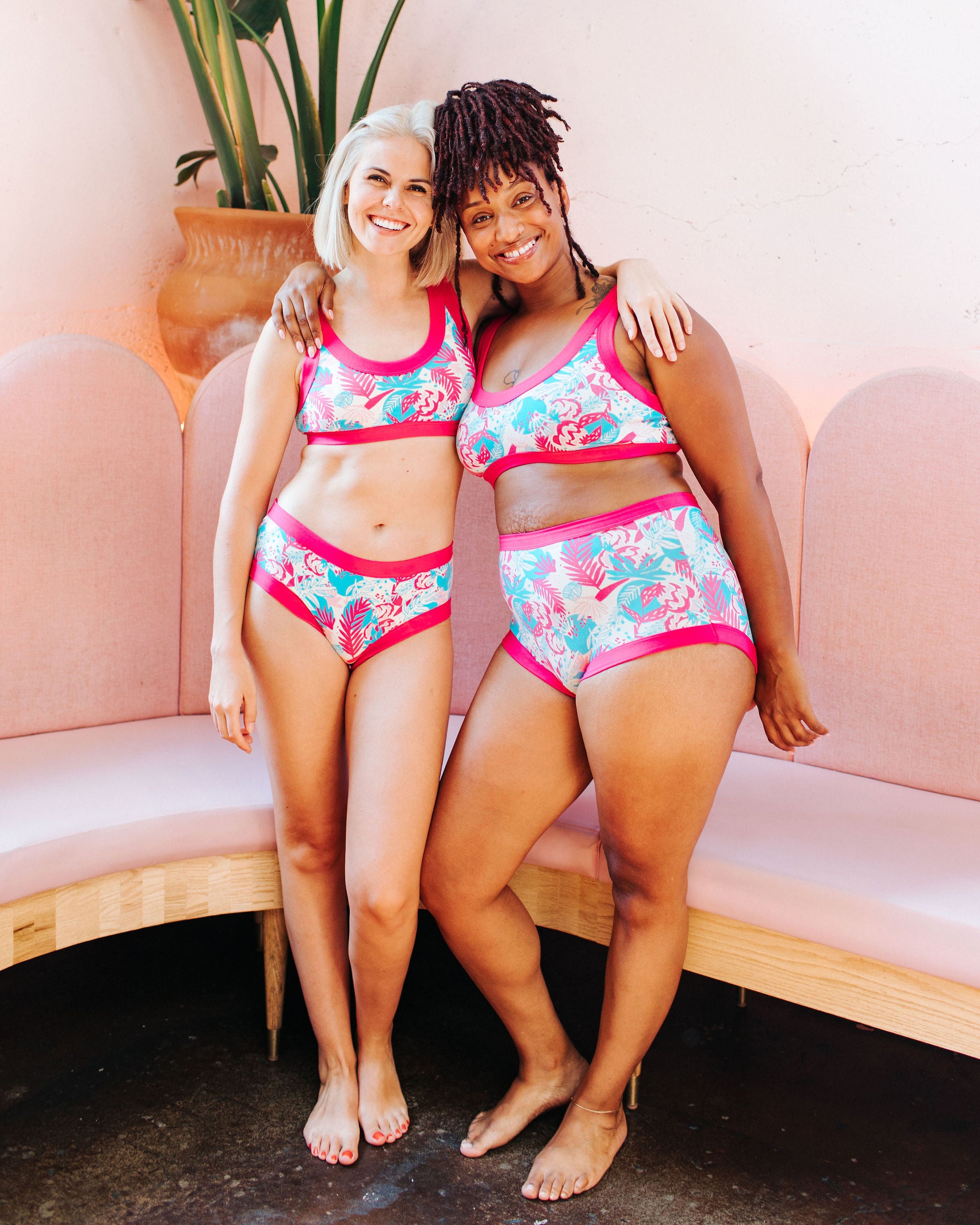 Two models smiling while wearing sets of Thunderpants Hipster and Sky Rise style underwear and Bralettes in Finding Flamingos - pink and blue Miami-inspired print.
