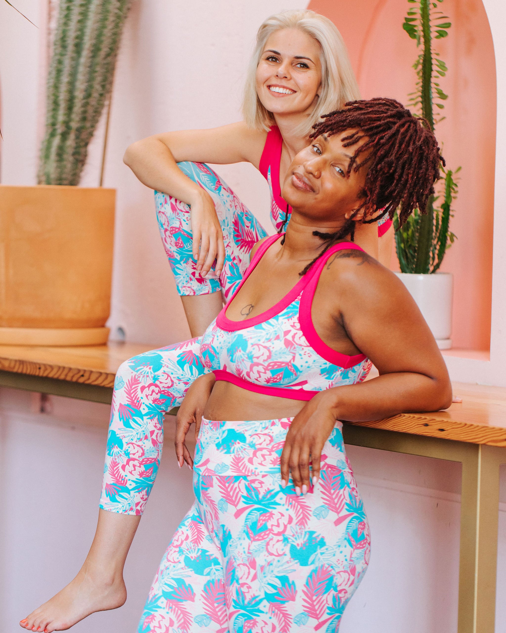 Two models wearing sets of Thunderpants Bralettes and 3/4 Length Leggings in Finding Flamingos - pink and blue Miami-inspired print.