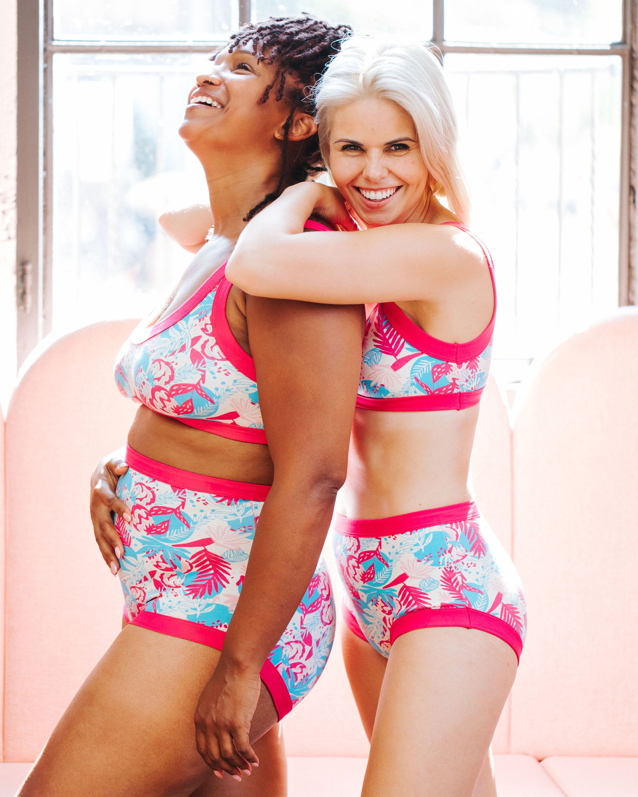 Two models laughing together wearing sets of Thunderpants Original and Sky Rise style underwear and Bralettes in Finding Flamingos - blue and pink Miami-style print.