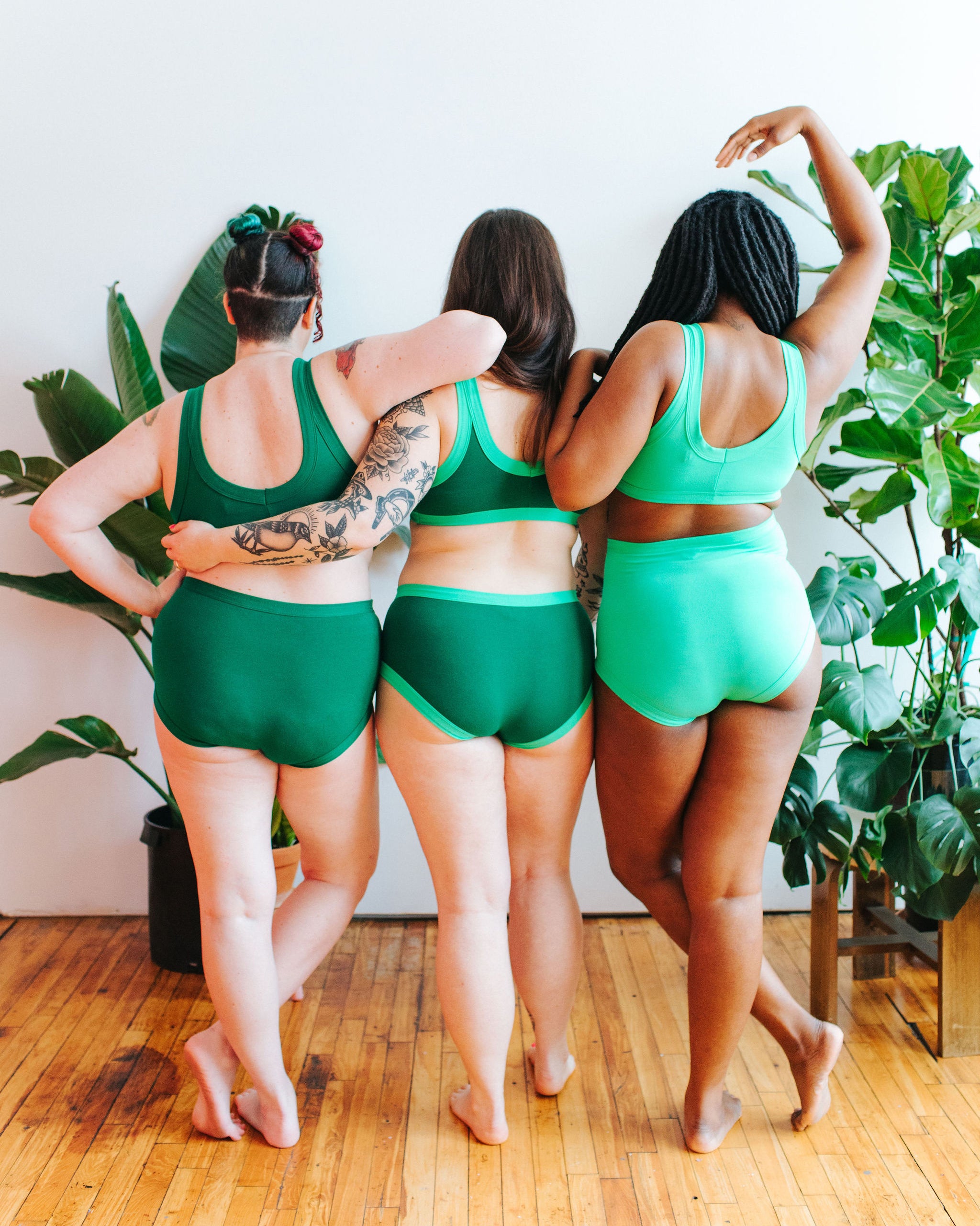 Three models standing with their backs to the camera wearing various styles of Emerald Green, Lime Squeeze, and Sour Apple.