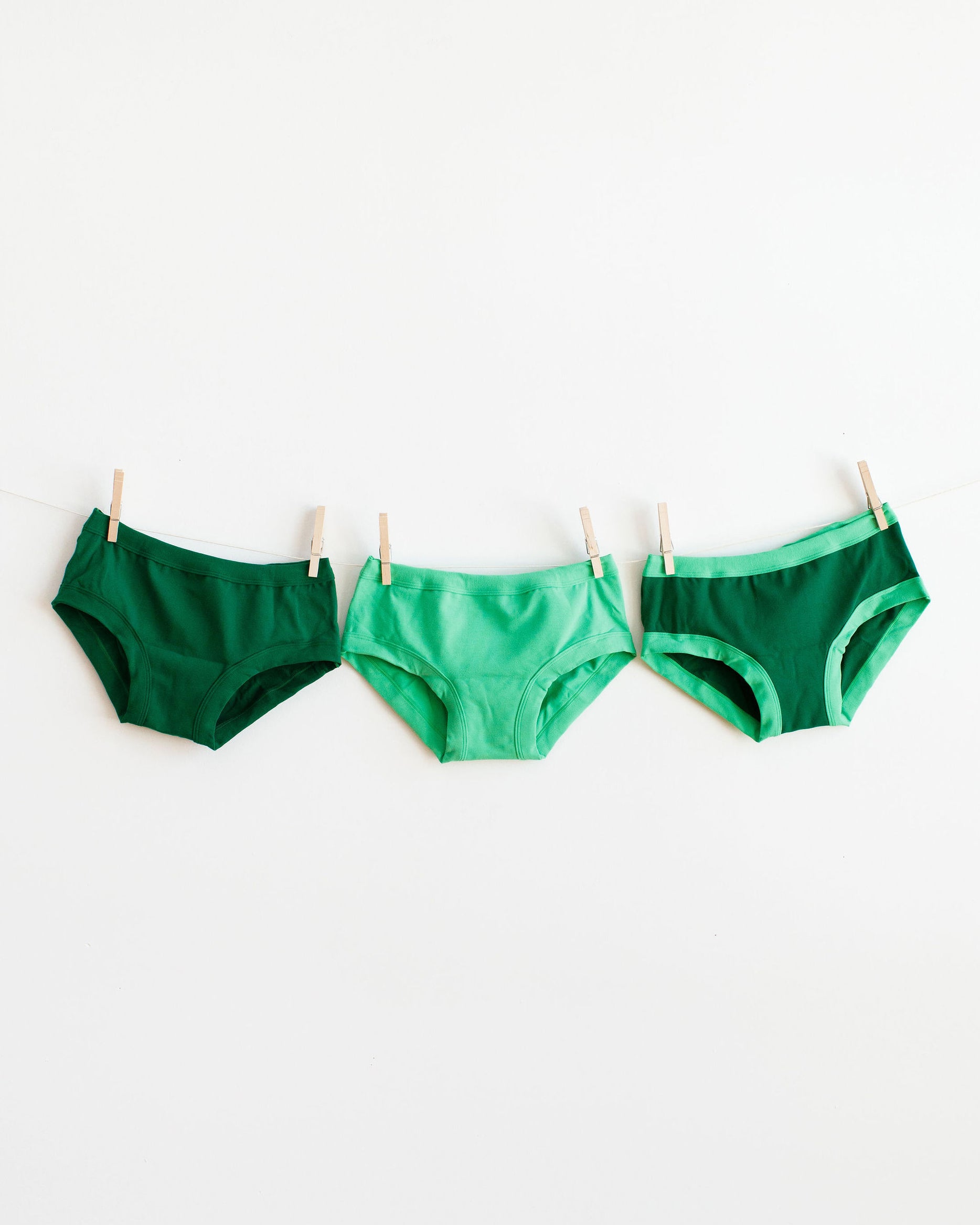 Three Hipster style underwear in different green colors hanging on a white wall.