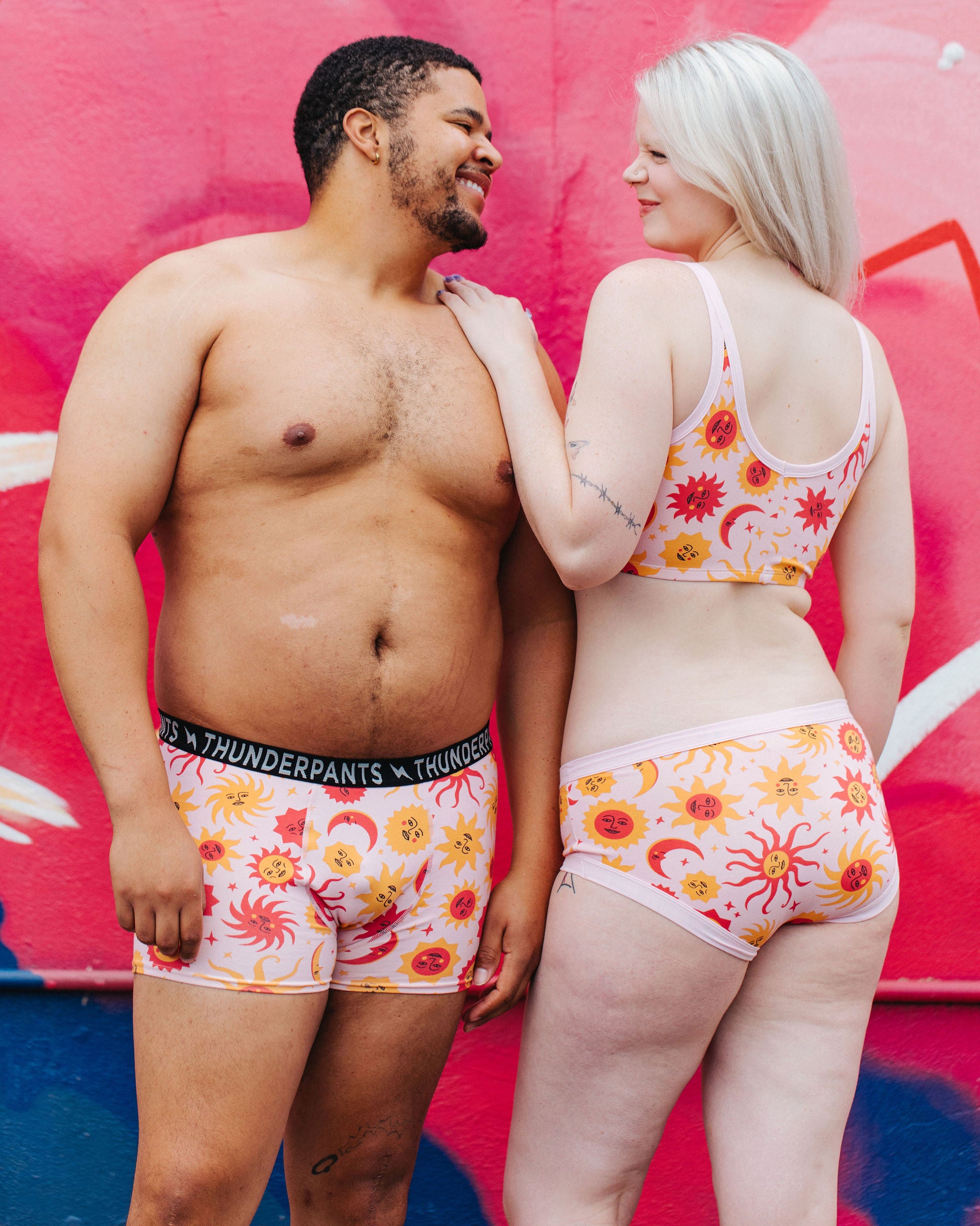 Two models wearing Thunderpants Hipster style underwear, Longline Bra, and Boxer Brief style underwear in Luna y Sol print - pink, yellow, and orange suns and moons.