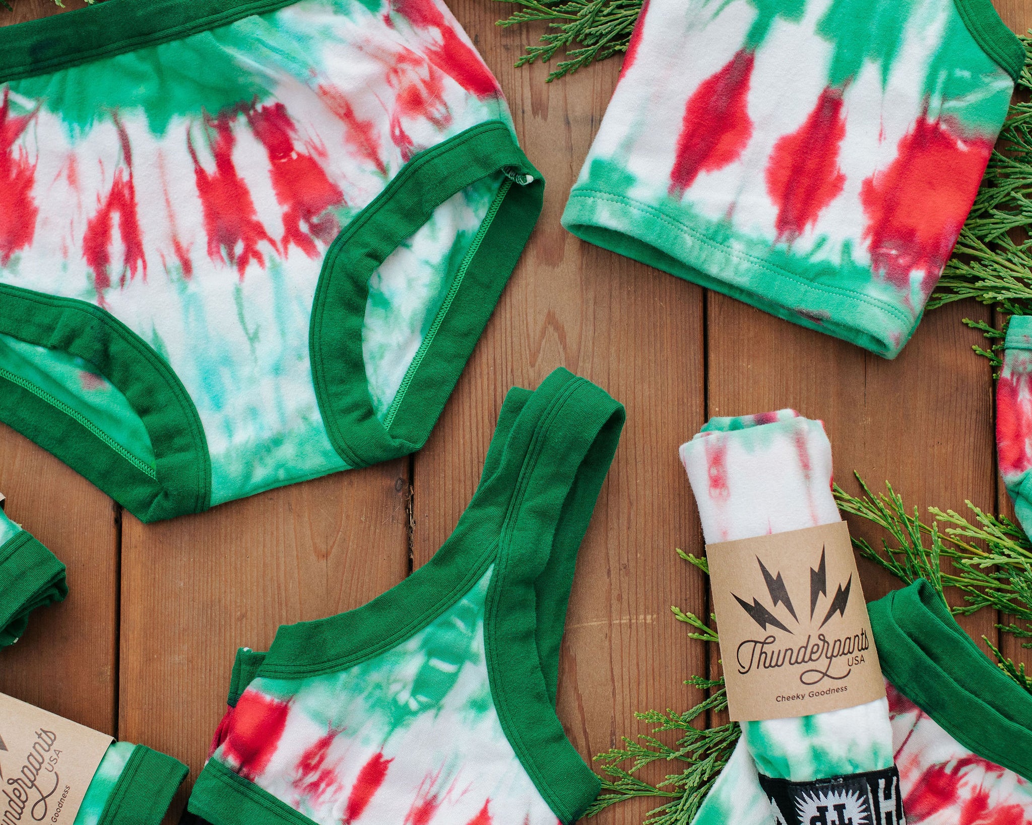 Flat lay of various styles of Thunderpants in Holiday Dye - red and green die dye with green binding. 