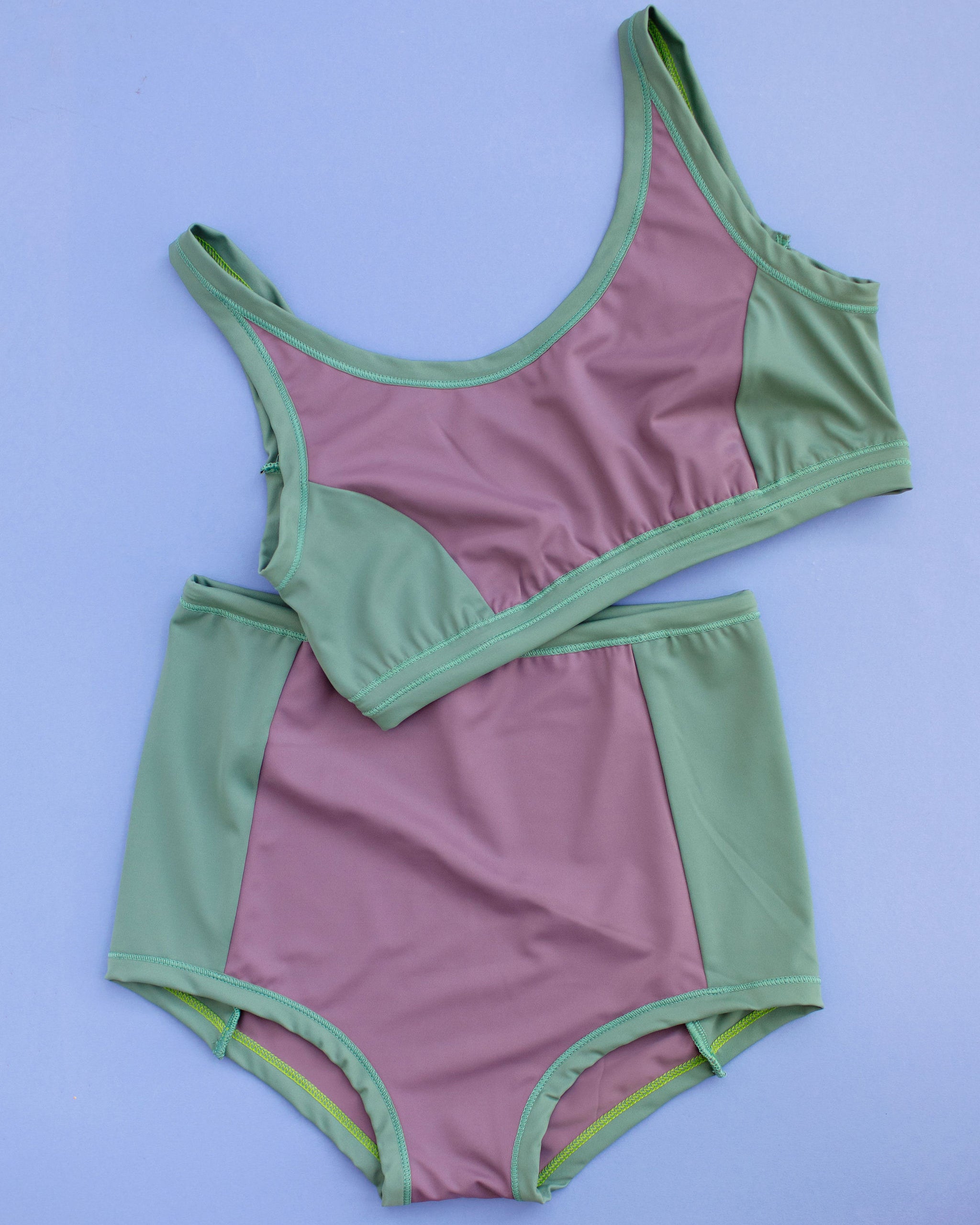 Flat lay of Thunderpants Swim Panel Top and Sky Rise Swim Panel Bottoms in lavender and lichen green.