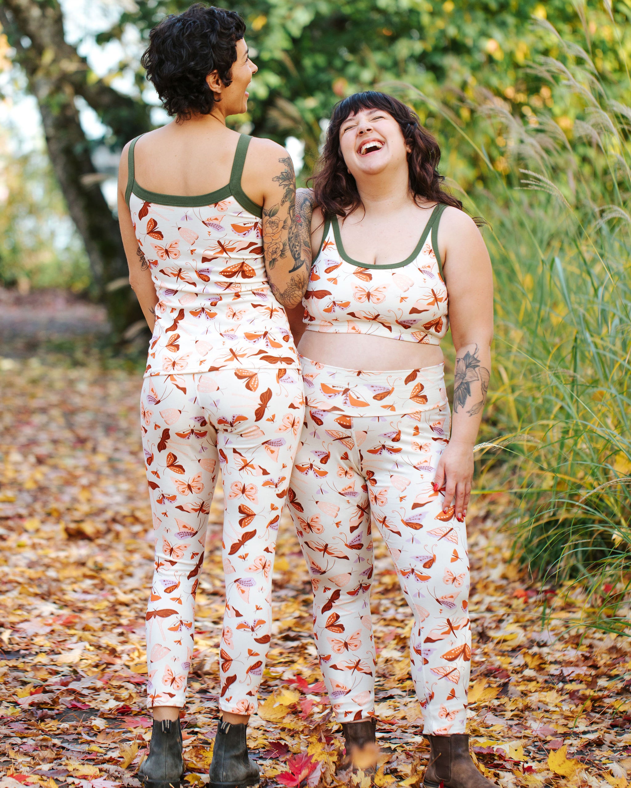Models wearing Thunderpants Ankle Length Leggings in Field Study: a moth print in red, orange, pink, and purple bound in green.