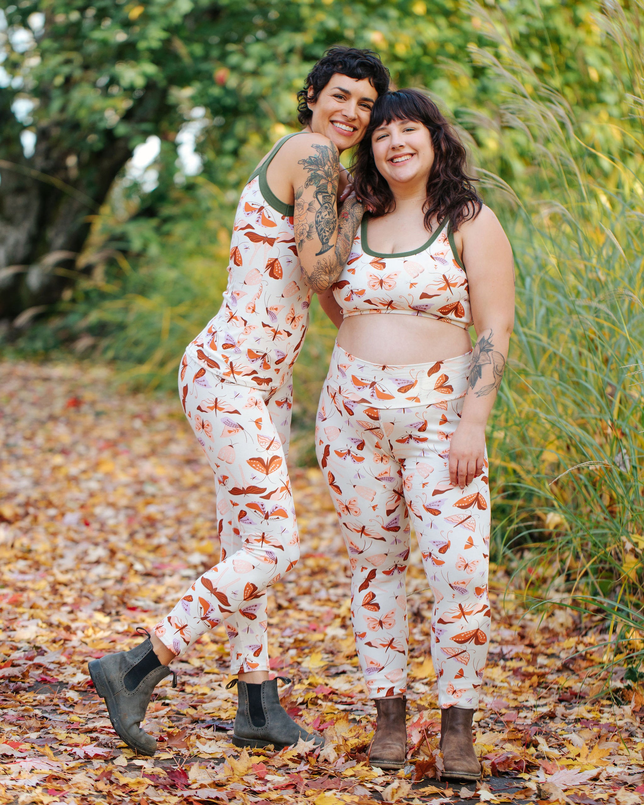 Models wearing Thunderpants Ankle Length Leggings in Field Study: a moth print in red, orange, pink, and purple bound in green.