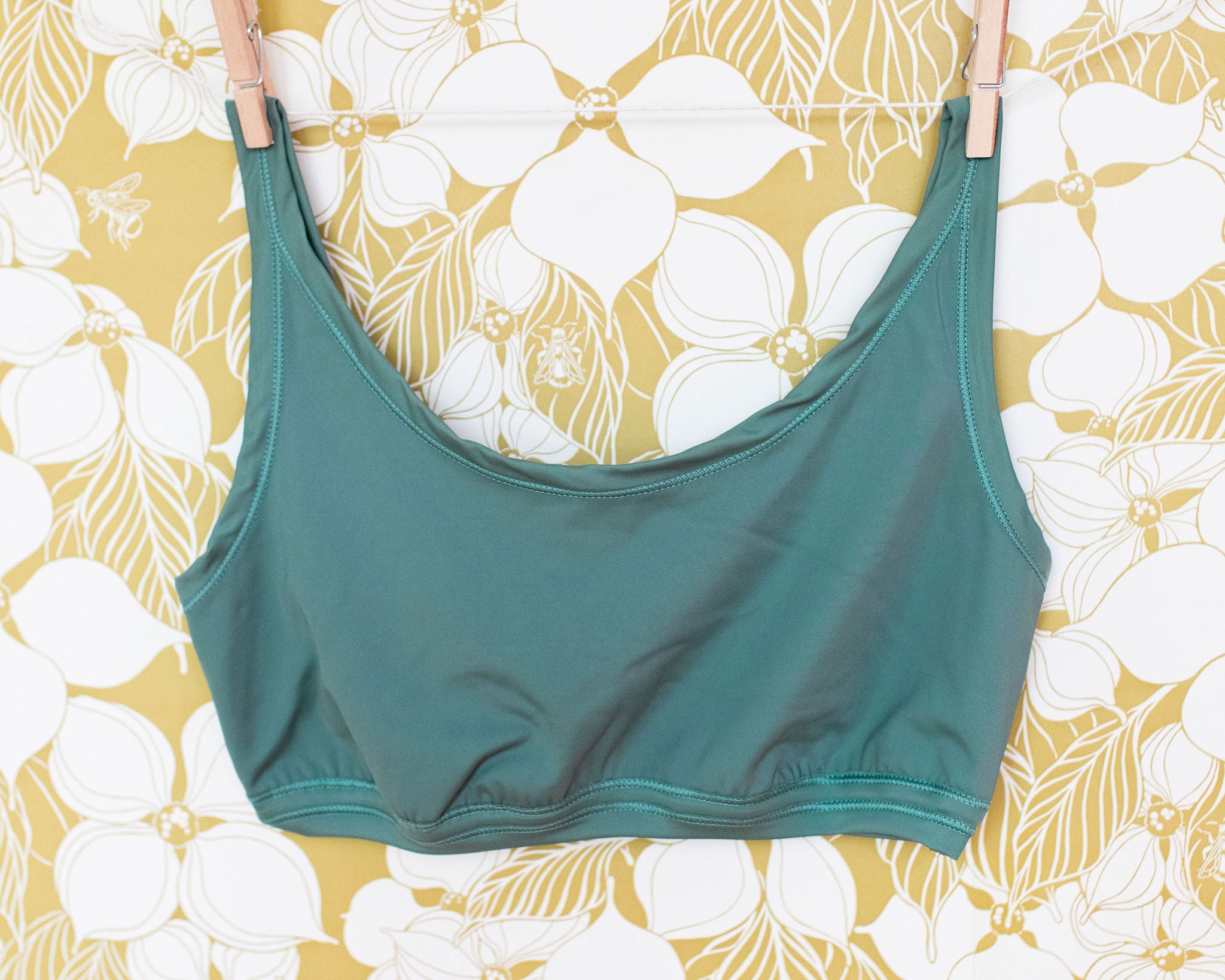 Swimwear Top in Lichen Green hanging with clothes pins on a floral wall.