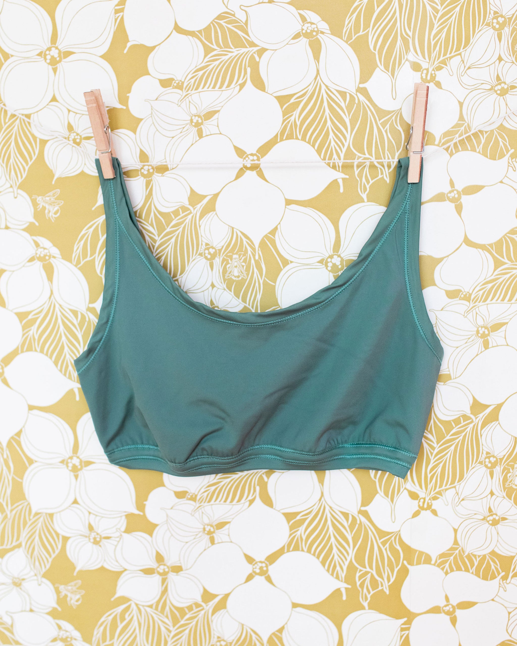 Swimwear Top in Lichen Green hanging with clothes pins on a floral wall.