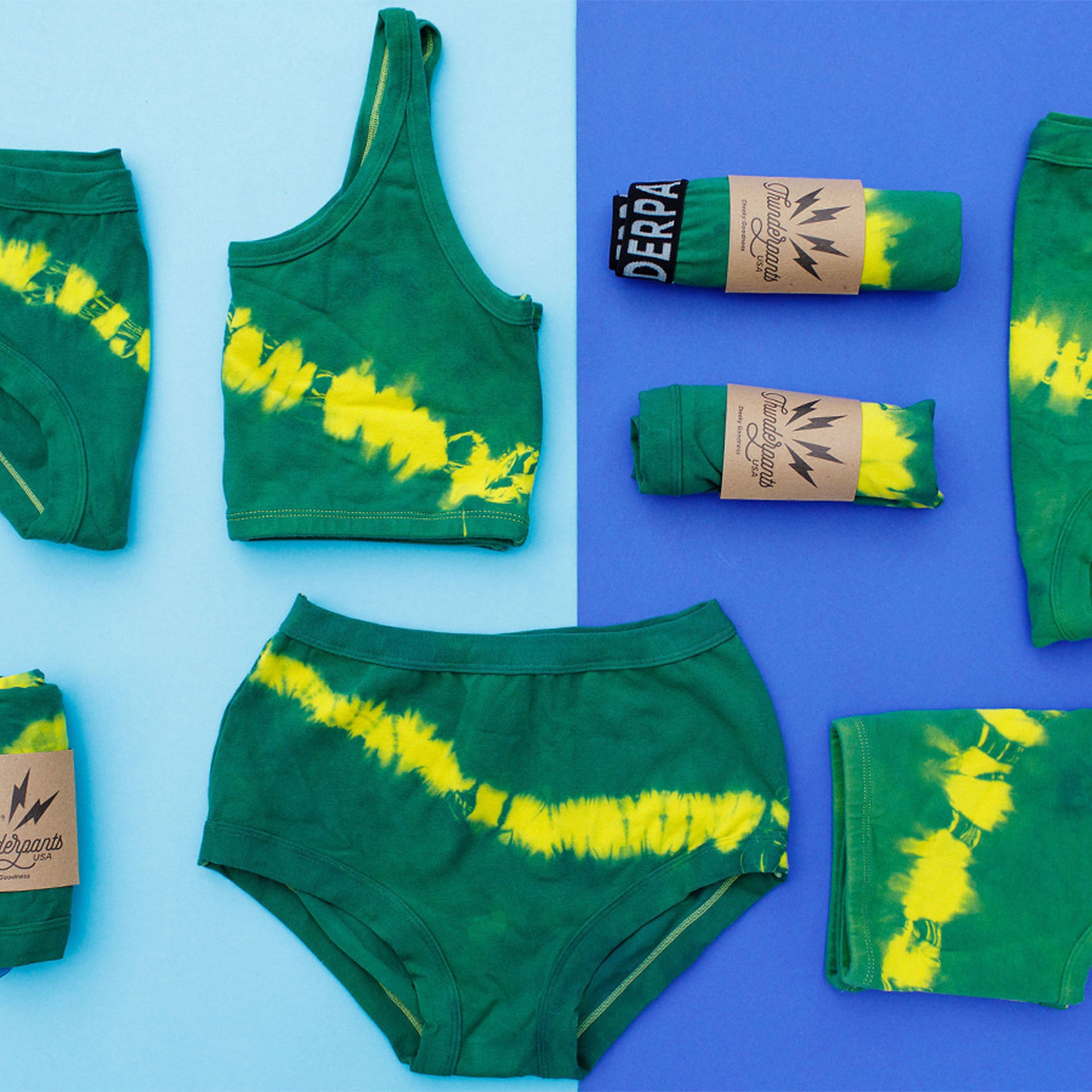 Flat lay of multiple Thunderpants styles in Lighting Bolt hand dye - green/blue color with yellow stripe. 