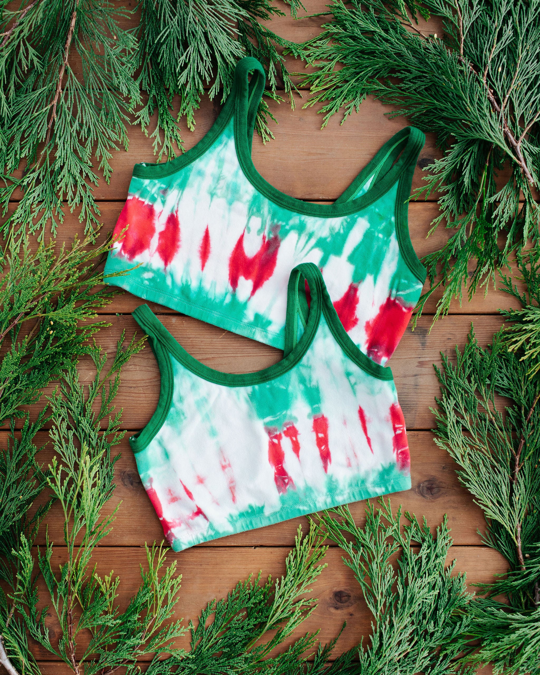 Flay lay of two Thunderpants Longline Bra in Holiday Dye - red and green tie dye with green binding. 