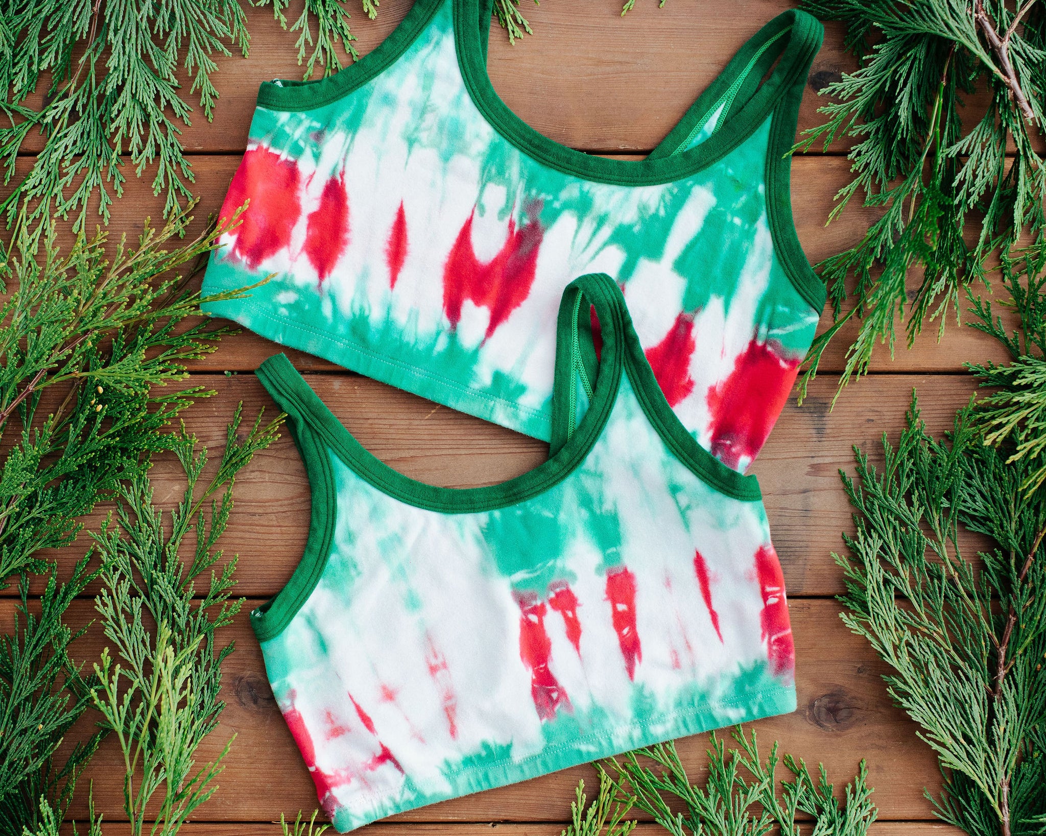 Flay lay of two Thunderpants Longline Bra in Holiday Dye - red and green tie dye with green binding. 